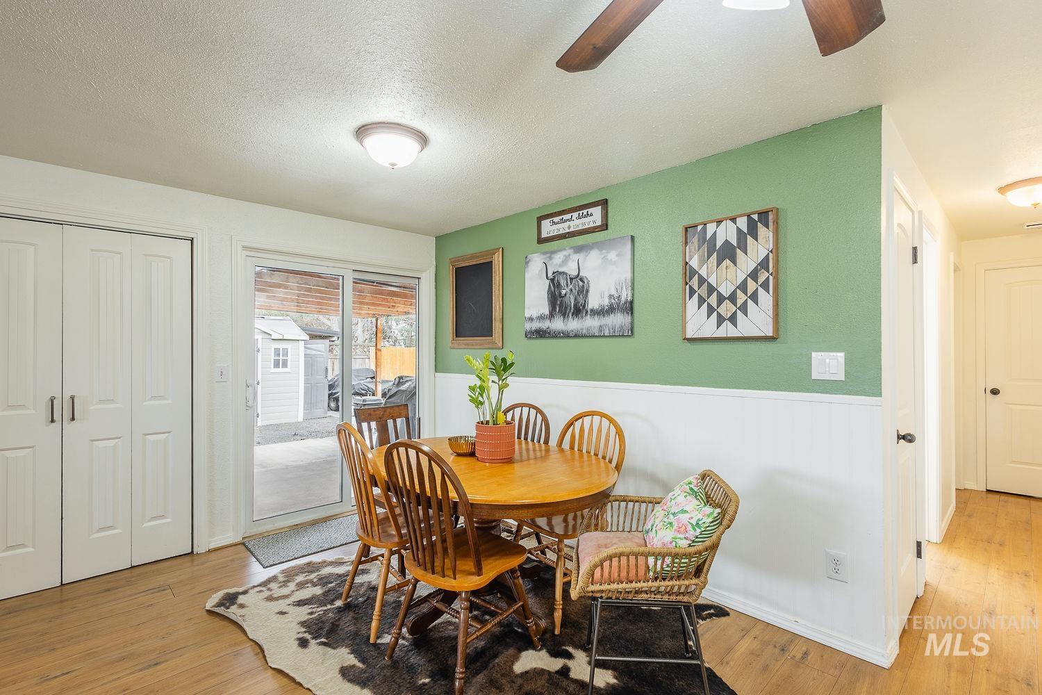 Dining space with ceiling fan, a wainscoted wall, light wood finished floors, and a textured ceiling