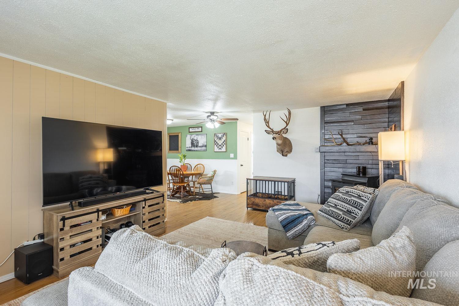 Living area with light wood-style flooring, ceiling fan, a fireplace, and a textured ceiling