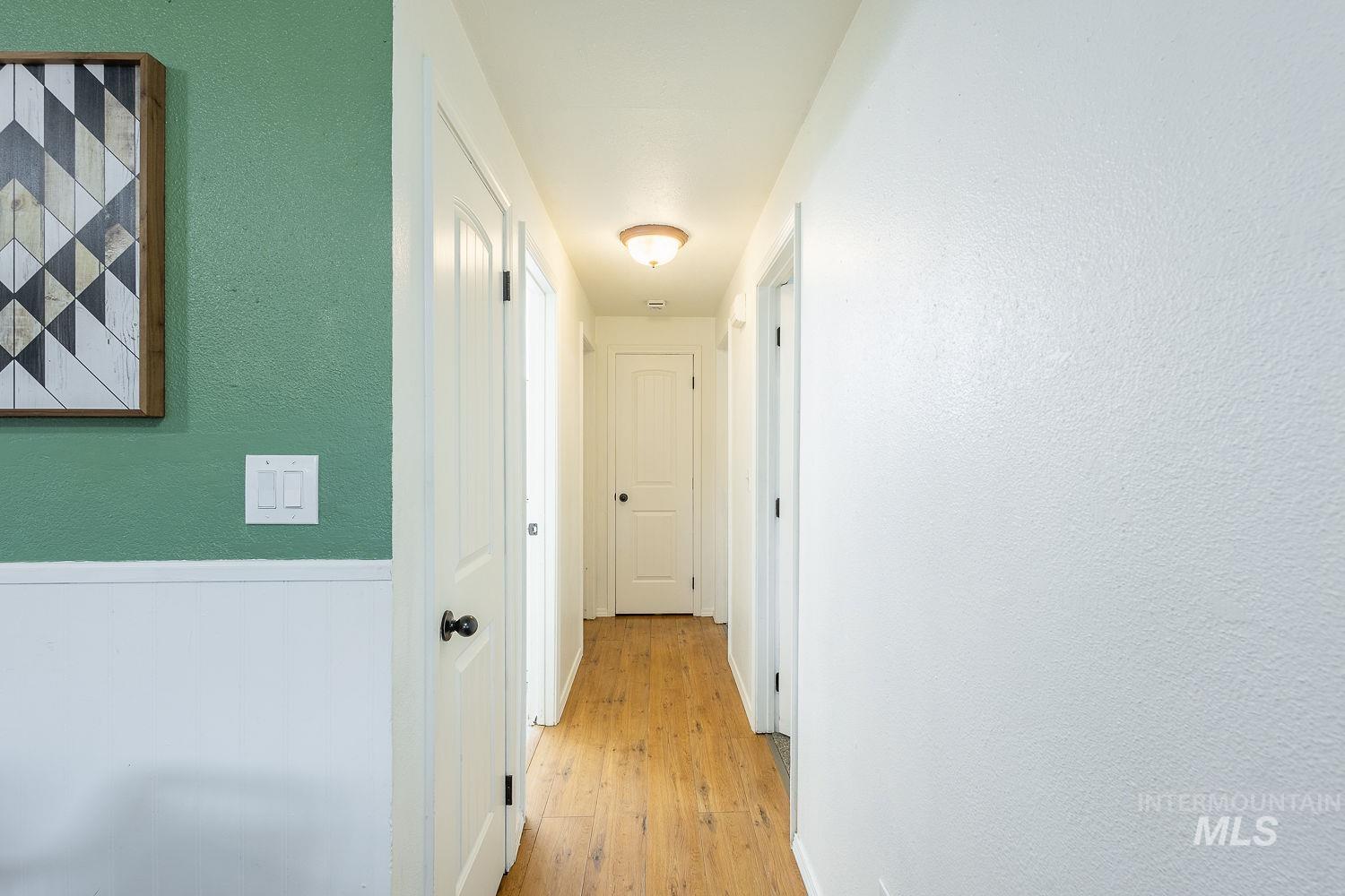 Hallway featuring light wood-type flooring, a textured wall, and a wainscoted wall