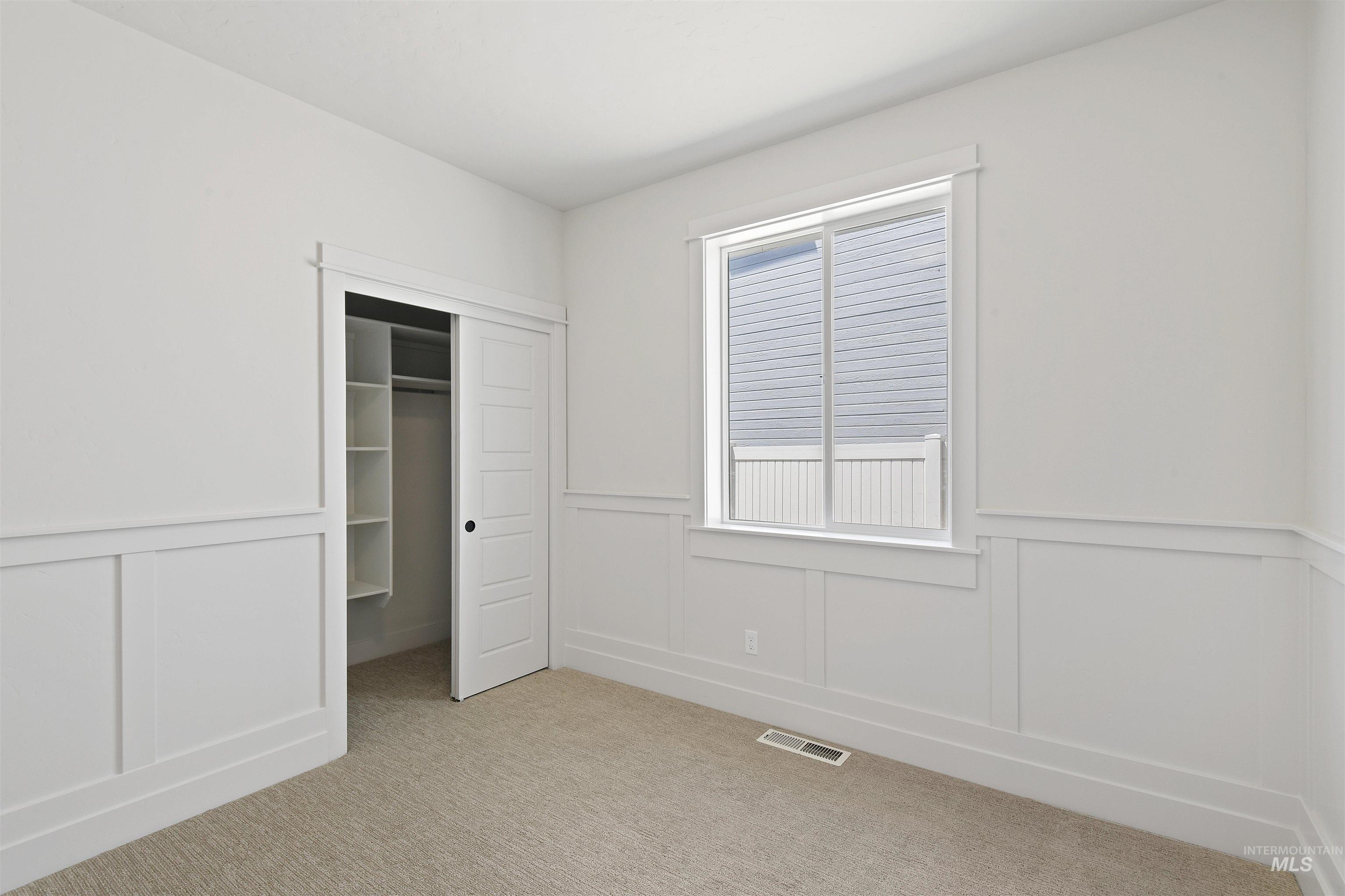 Unfurnished bedroom with light colored carpet, a decorative wall, a wainscoted wall, and a closet