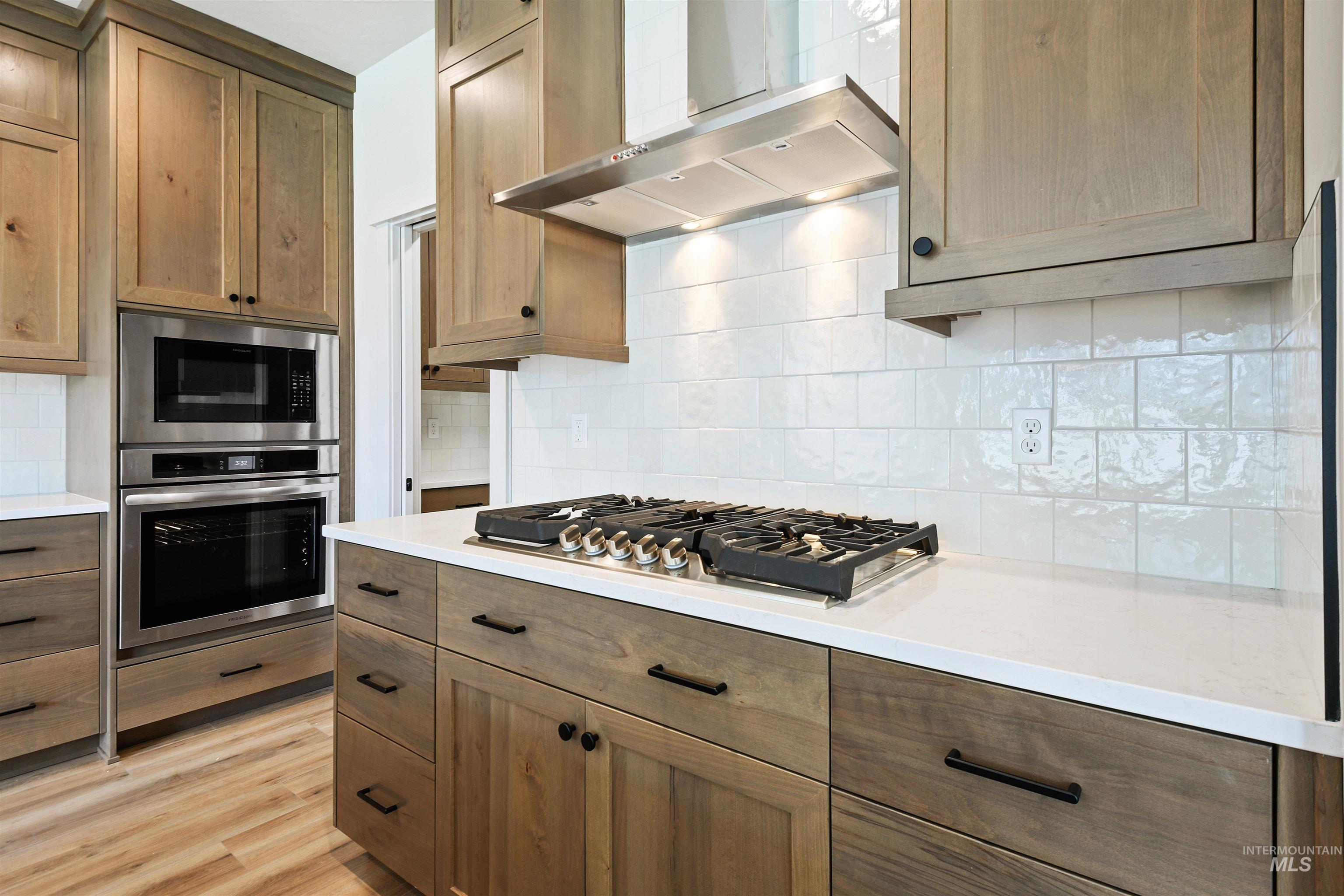 Kitchen featuring appliances with stainless steel finishes, wall chimney range hood, decorative backsplash, and light countertops