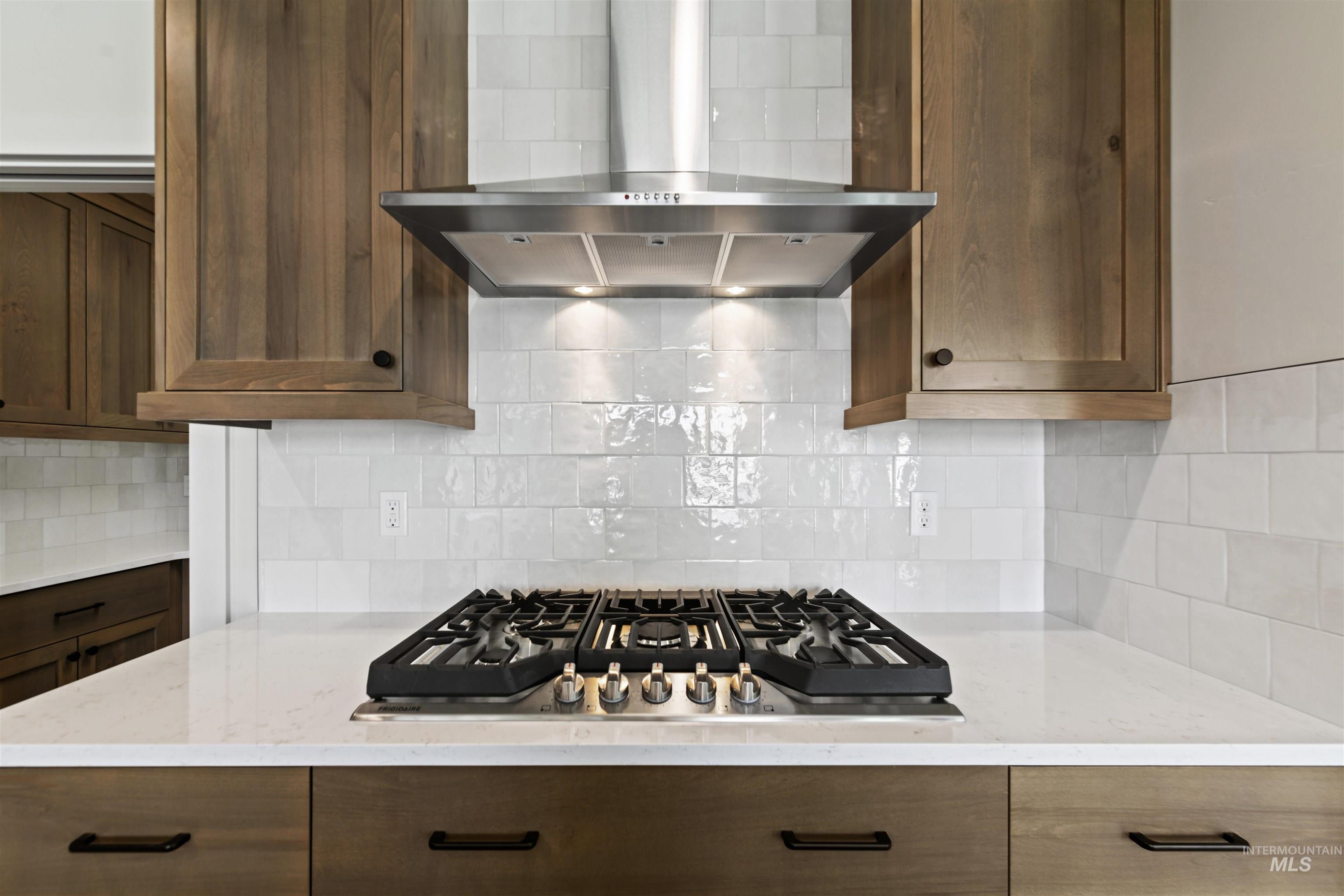 Kitchen with wall chimney range hood, stainless steel gas stovetop, tasteful backsplash, and light stone countertops