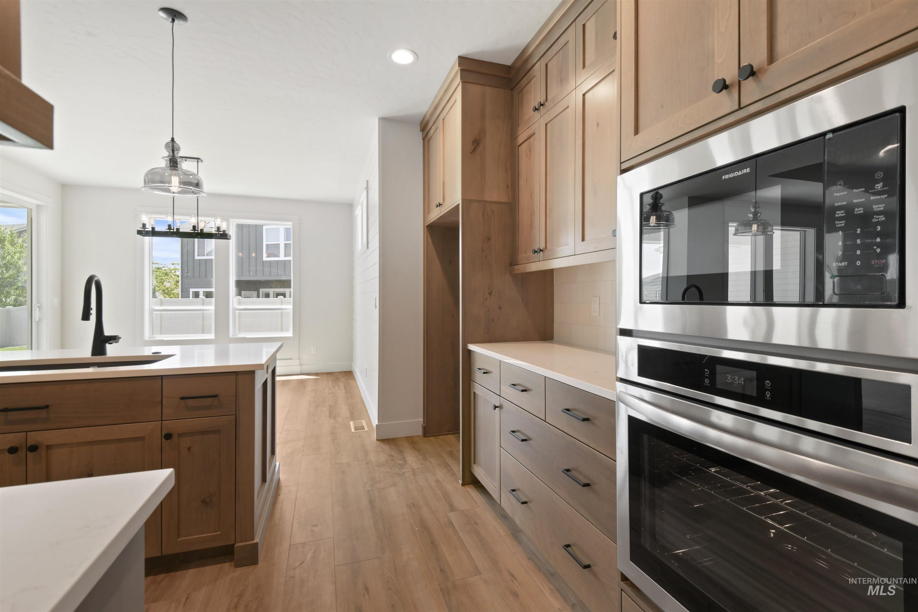 Kitchen featuring light countertops, light wood-style floors, appliances with stainless steel finishes, recessed lighting, and hanging light fixtures