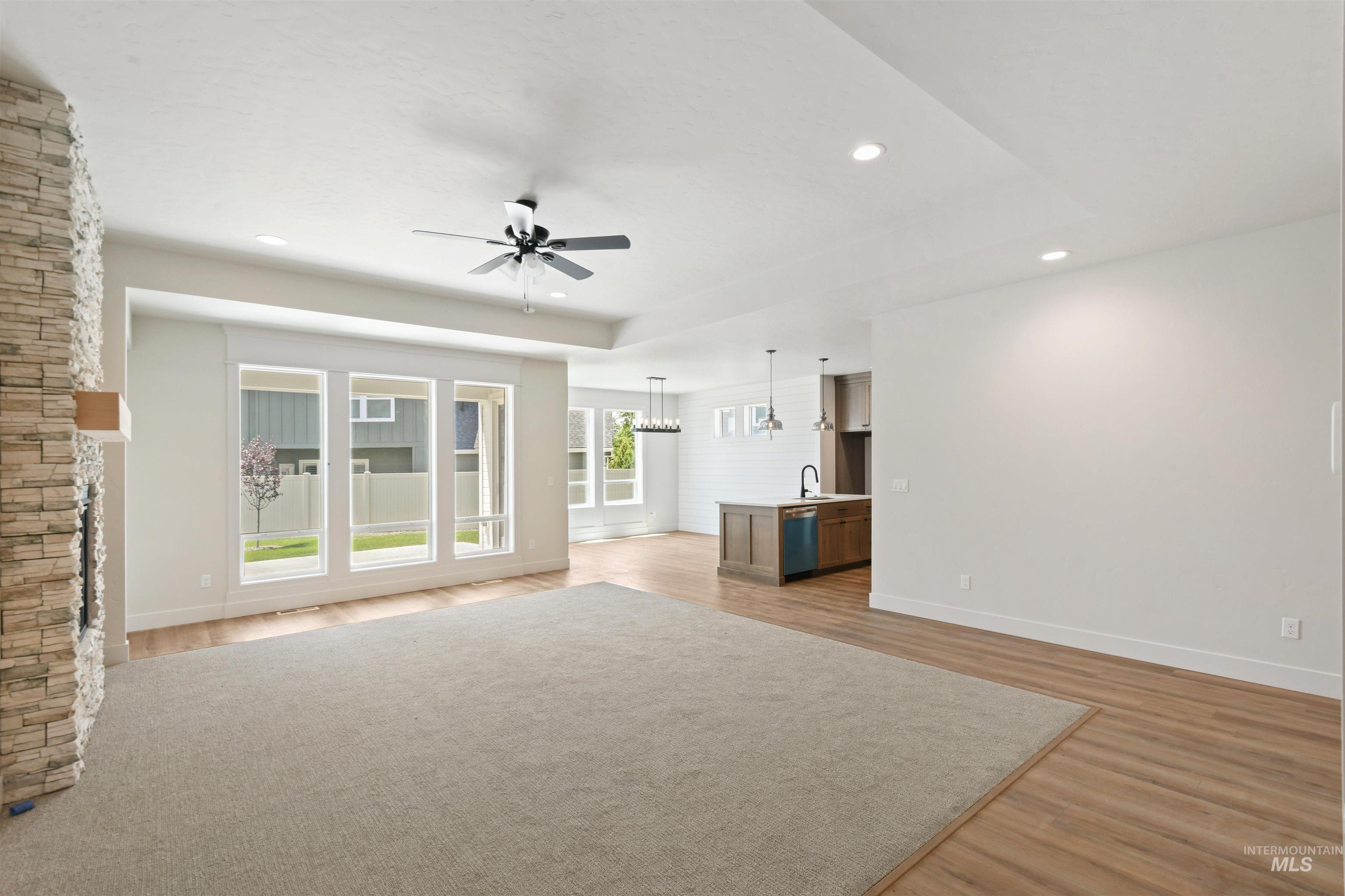 Unfurnished living room featuring ceiling fan, light wood-style floors, recessed lighting, a tray ceiling, and a chandelier