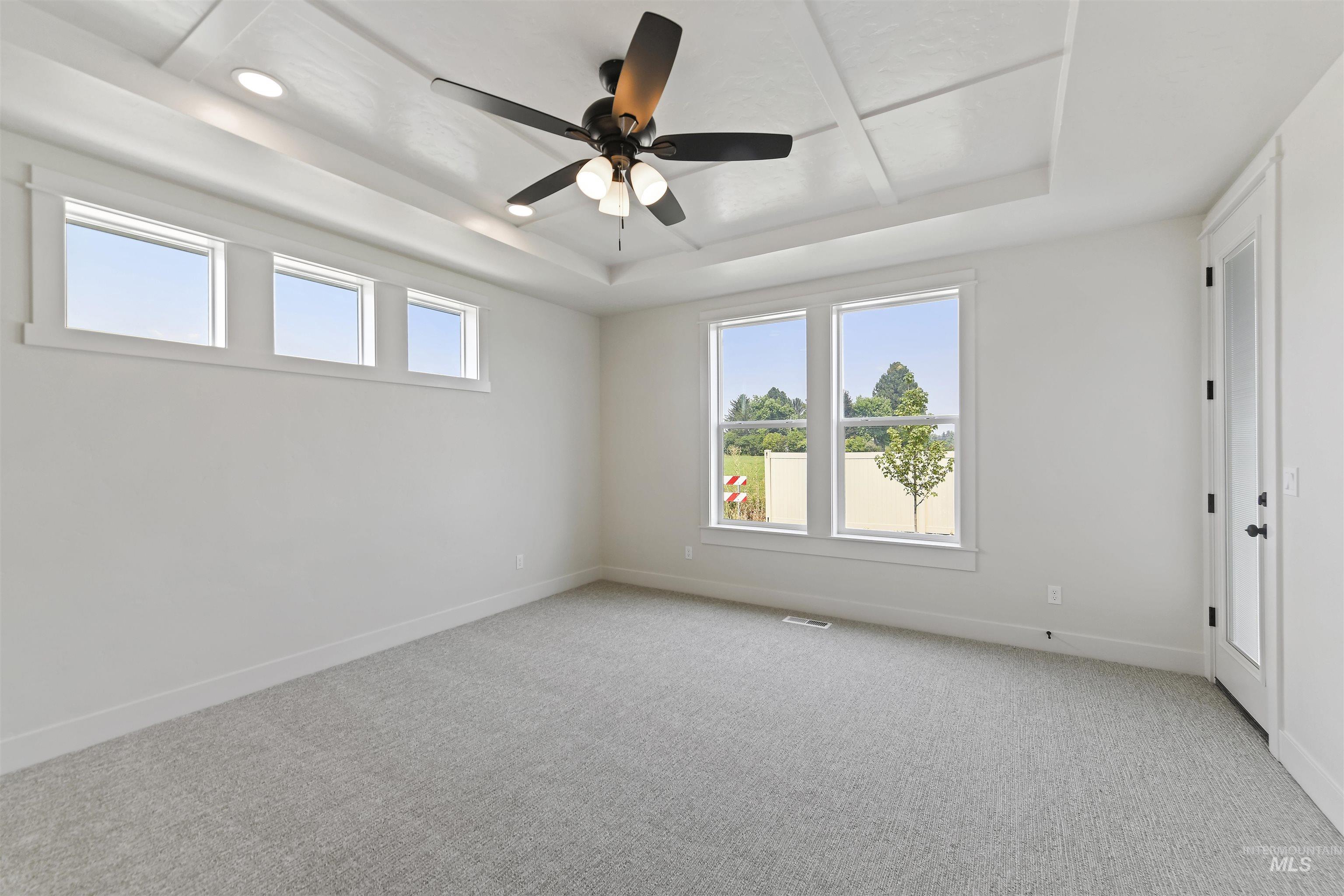 Empty room with a tray ceiling, light colored carpet, ceiling fan, and recessed lighting