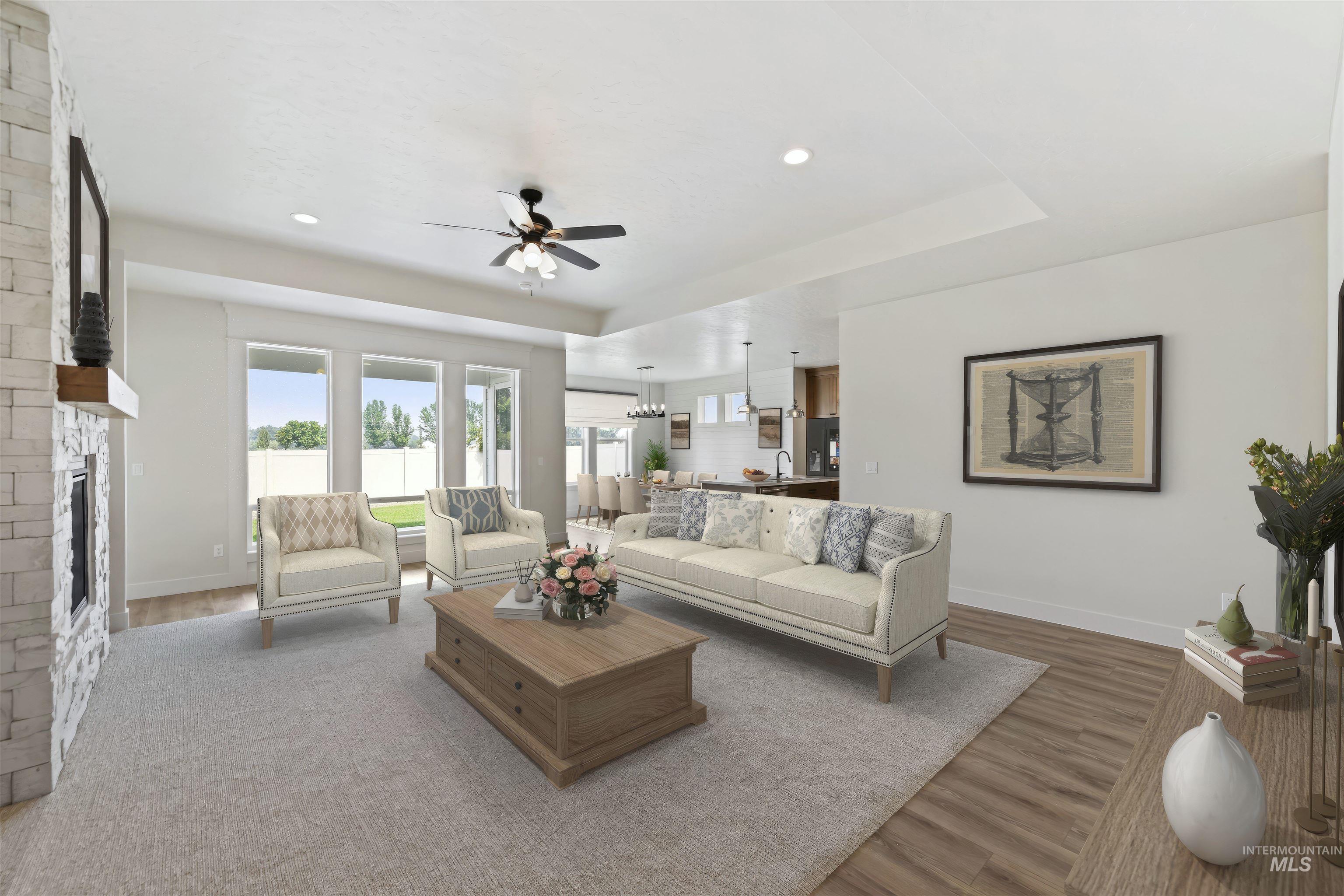 Living area featuring light wood-style flooring, a fireplace, a ceiling fan, a raised ceiling, and recessed lighting