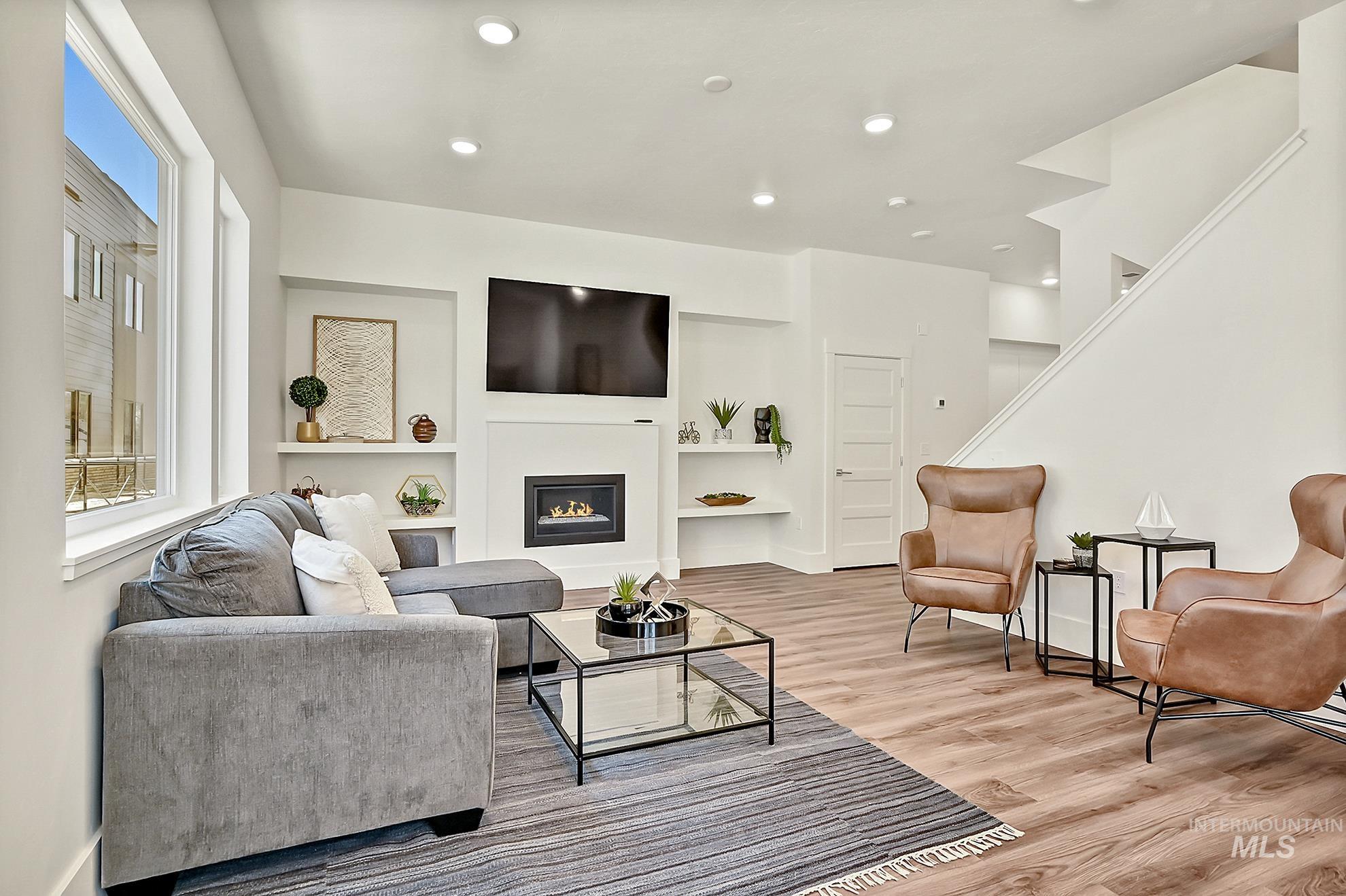 Living room with light wood-style flooring, a glass covered fireplace, built in shelves, and recessed lighting