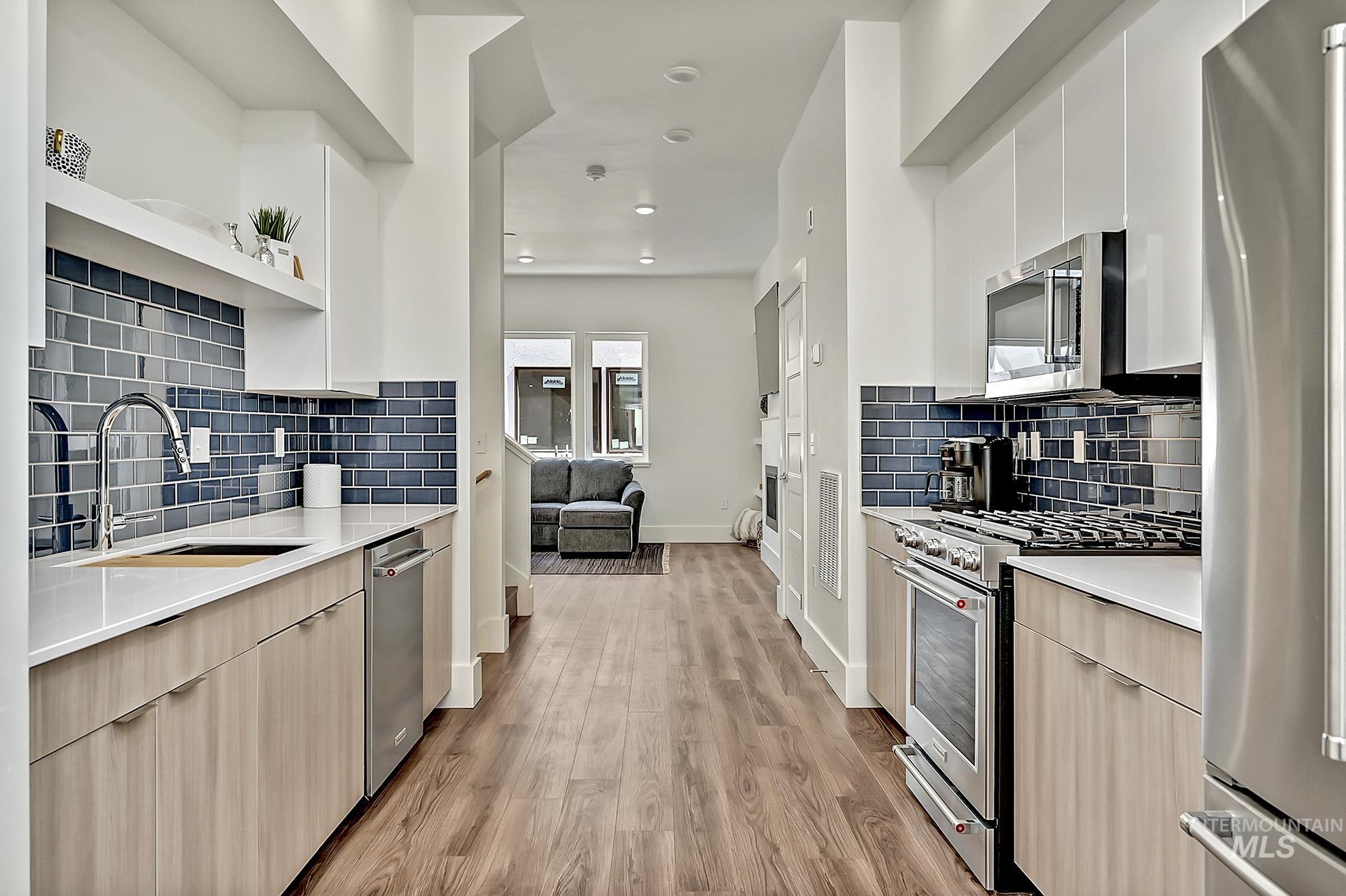 Kitchen featuring appliances with stainless steel finishes, open shelves, modern cabinets, light wood finished floors, and quartz counters