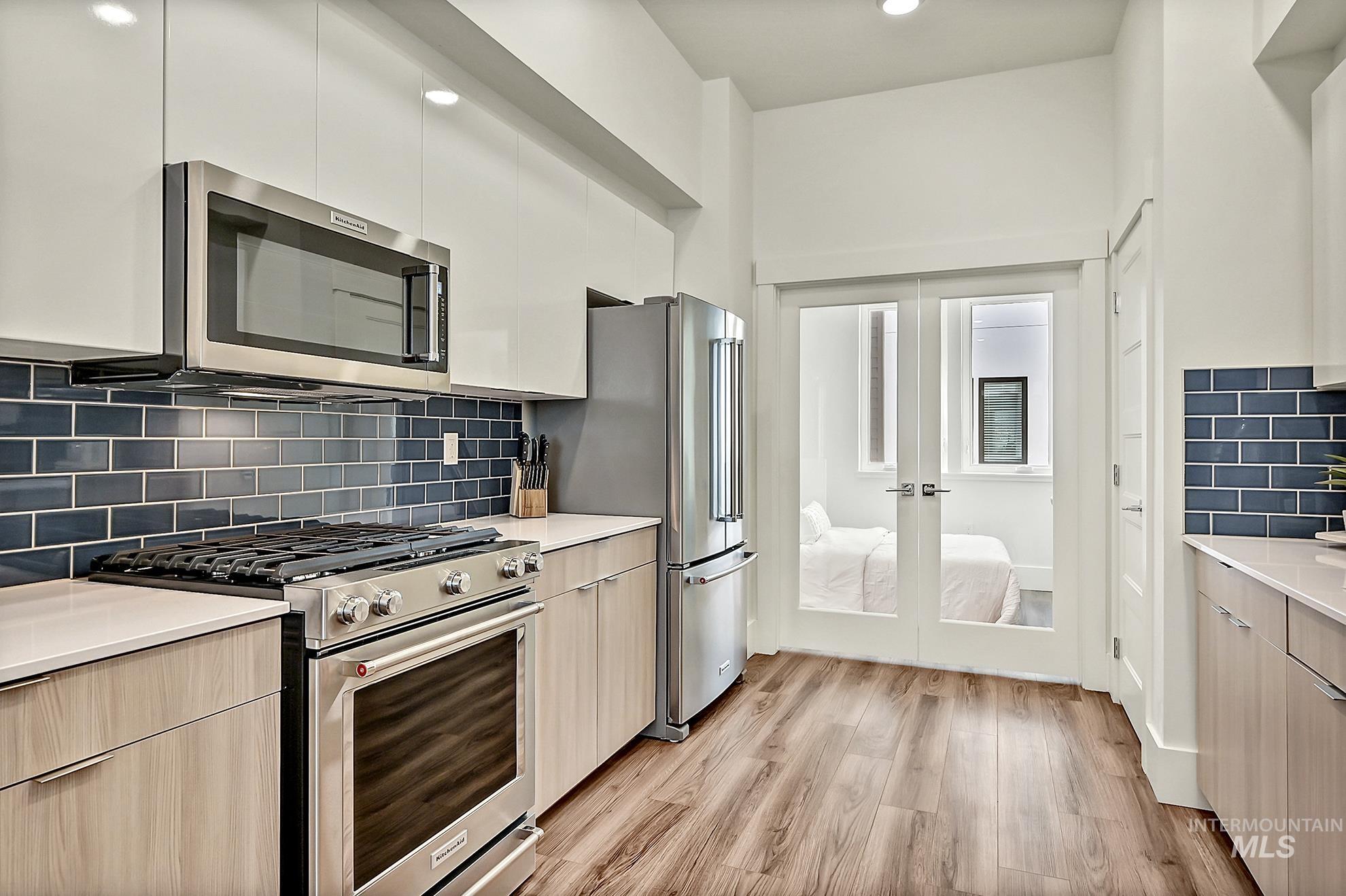 Kitchen featuring modern cabinets, decorative backsplash, stainless steel appliances, light wood-type flooring, and recessed lighting