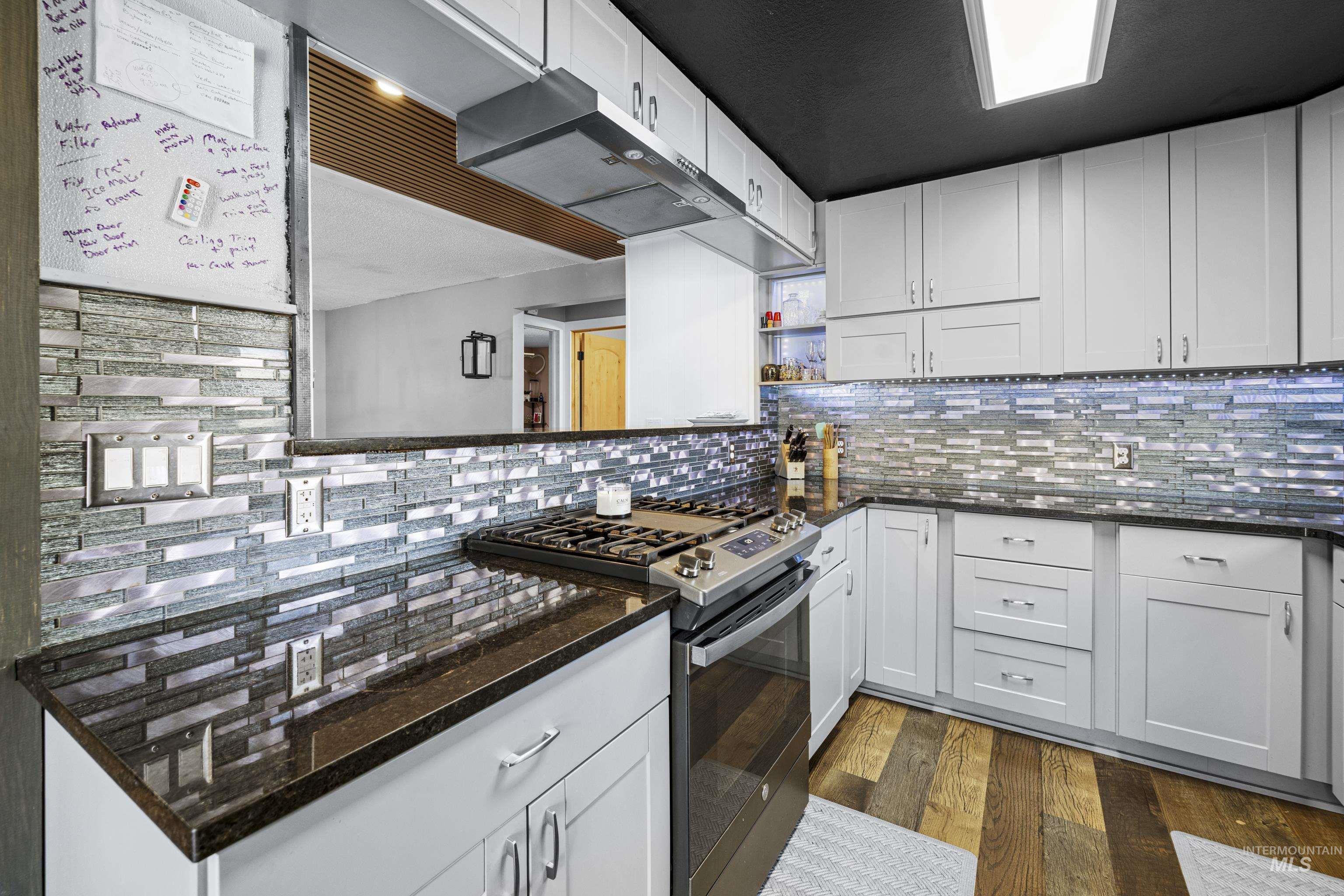 Kitchen featuring gas range, dark wood-type flooring, backsplash, and white cabinetry