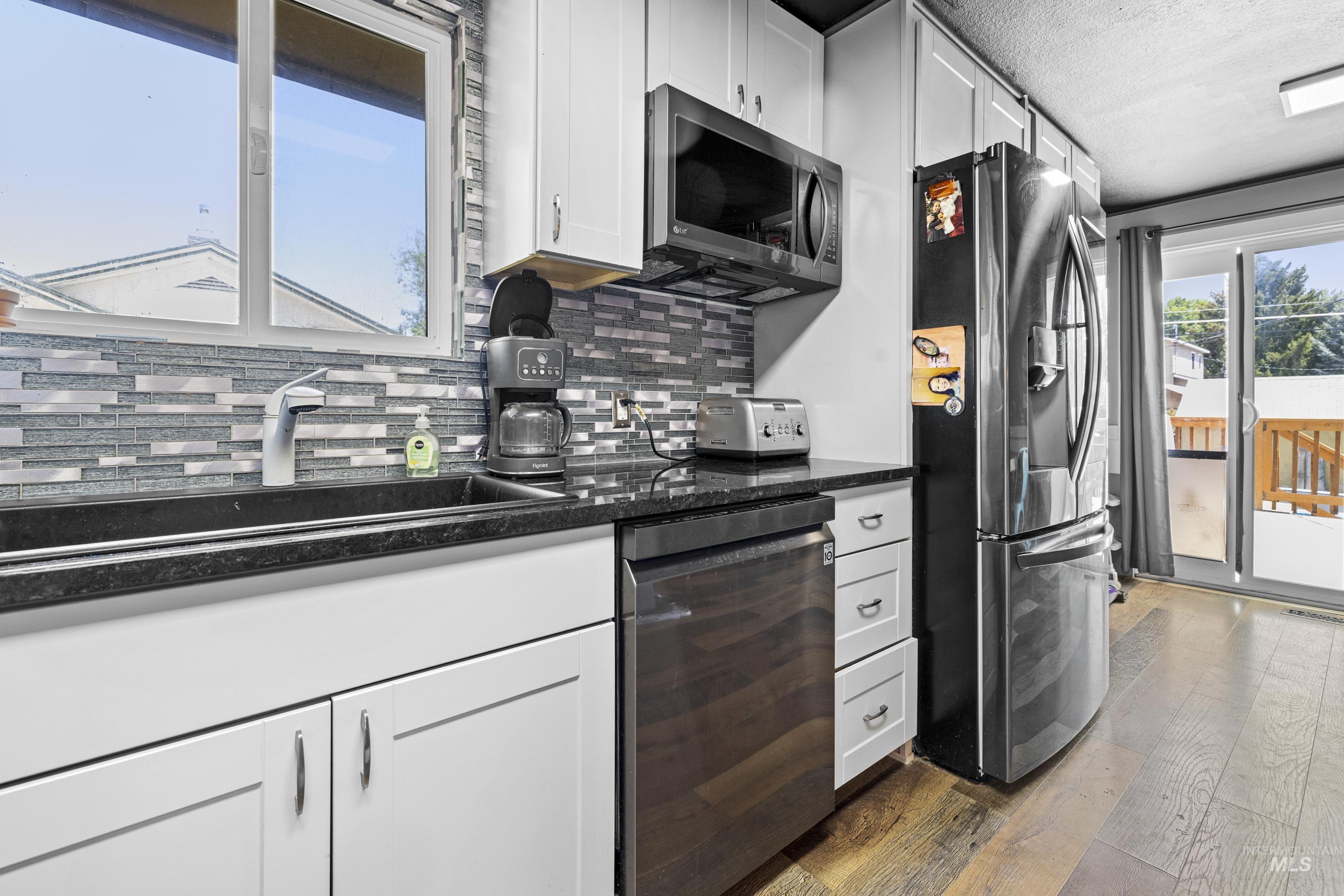 Kitchen with appliances with stainless steel finishes, decorative backsplash, hardwood / wood-style flooring, white cabinets, and a textured ceiling