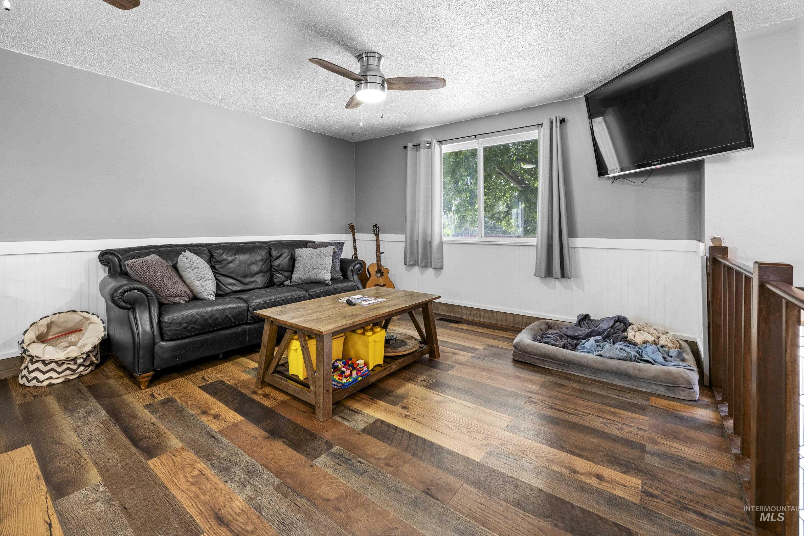 Living room featuring ceiling fan, a textured ceiling, a wainscoted wall, and wood finished floors