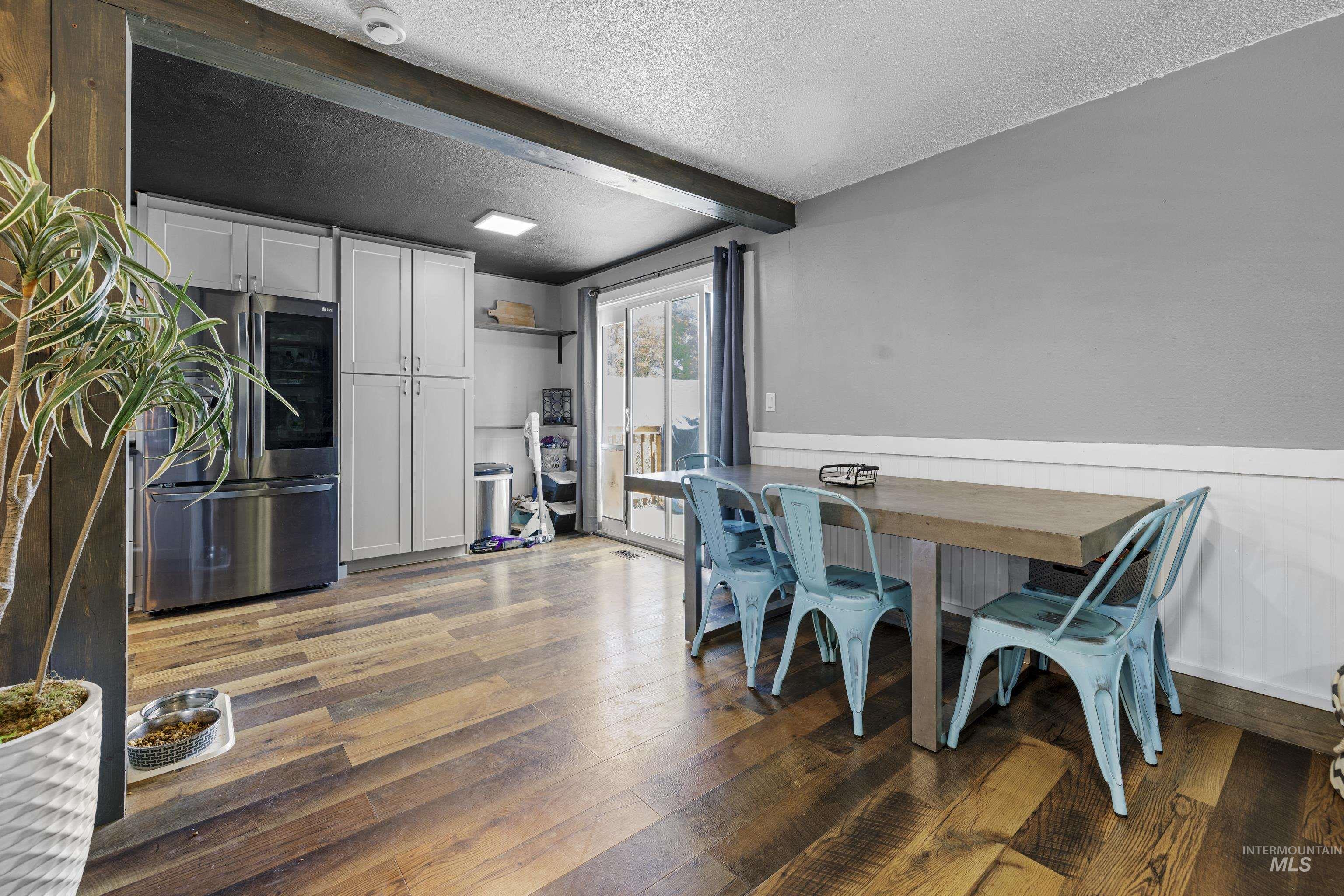 Dining room featuring a textured ceiling, beamed ceiling, hardwood / wood-style floors, and a wainscoted wall