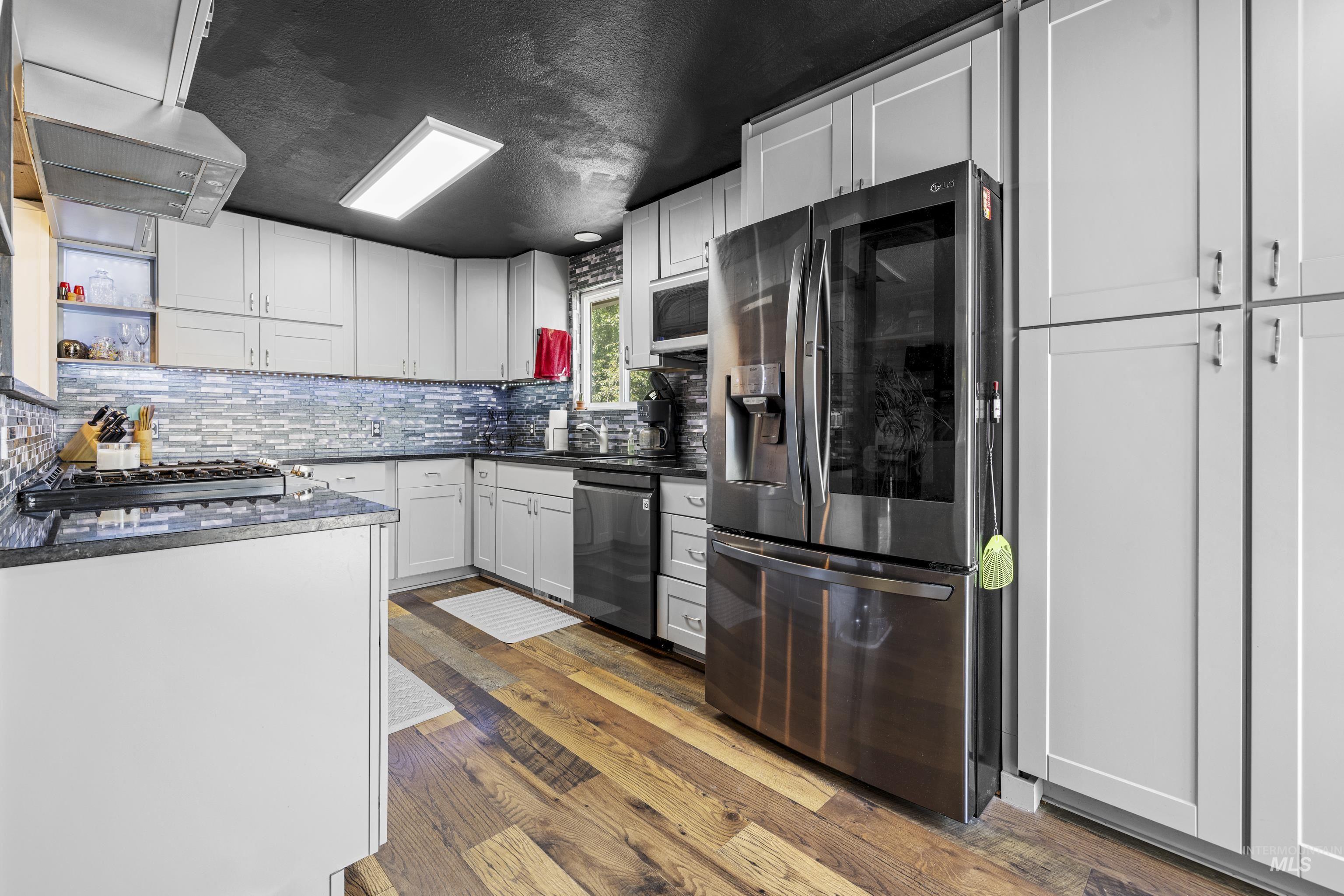 Kitchen with appliances with stainless steel finishes, tasteful backsplash, dark countertops, and wood finished floors