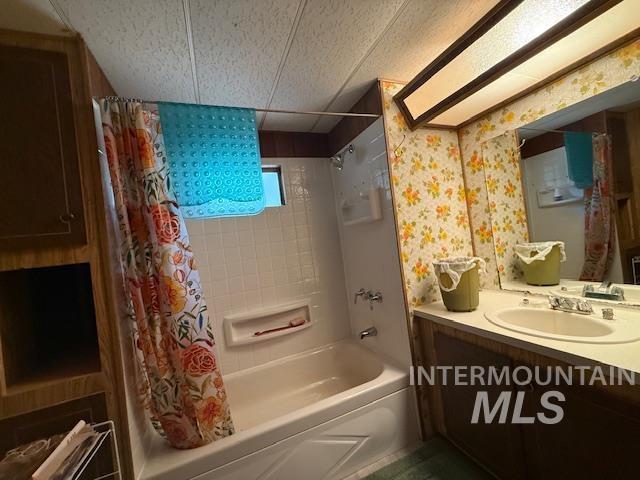 Bathroom with shower / bath combo with shower curtain, vanity, and wallpapered walls