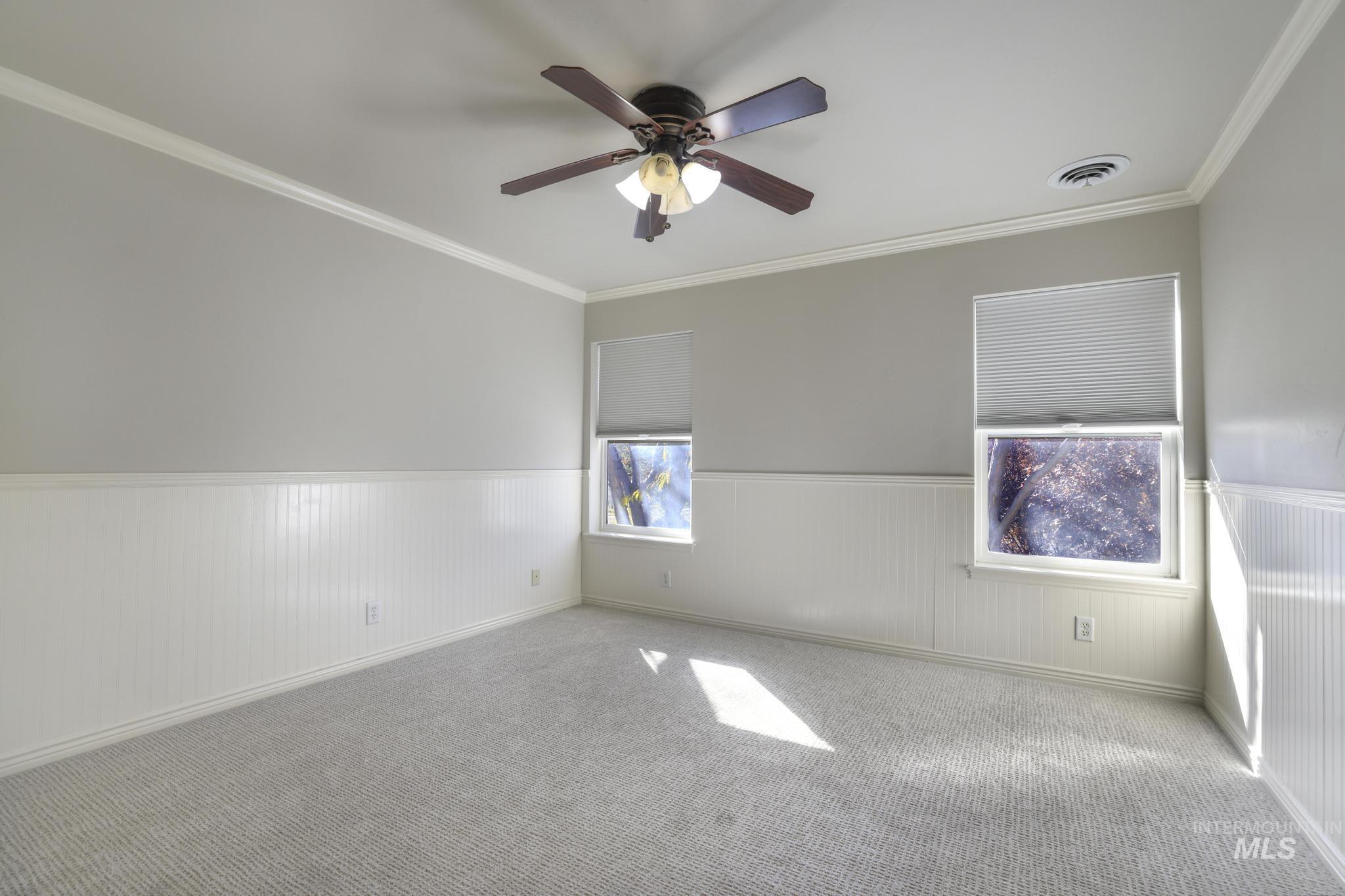 Empty room with crown molding, wainscoting, ceiling fan, and carpet