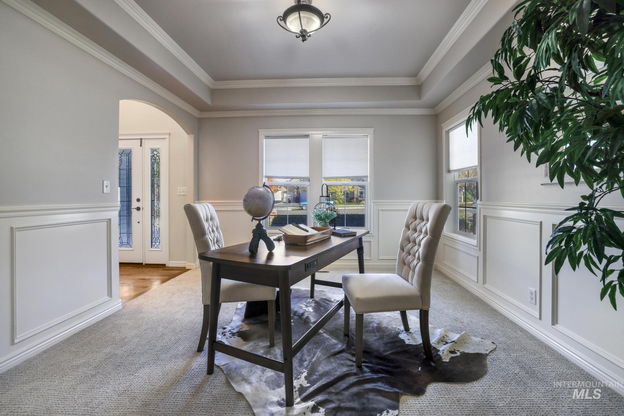 Office space featuring arched walkways, a raised ceiling, wainscoting, new carpet, and crown molding