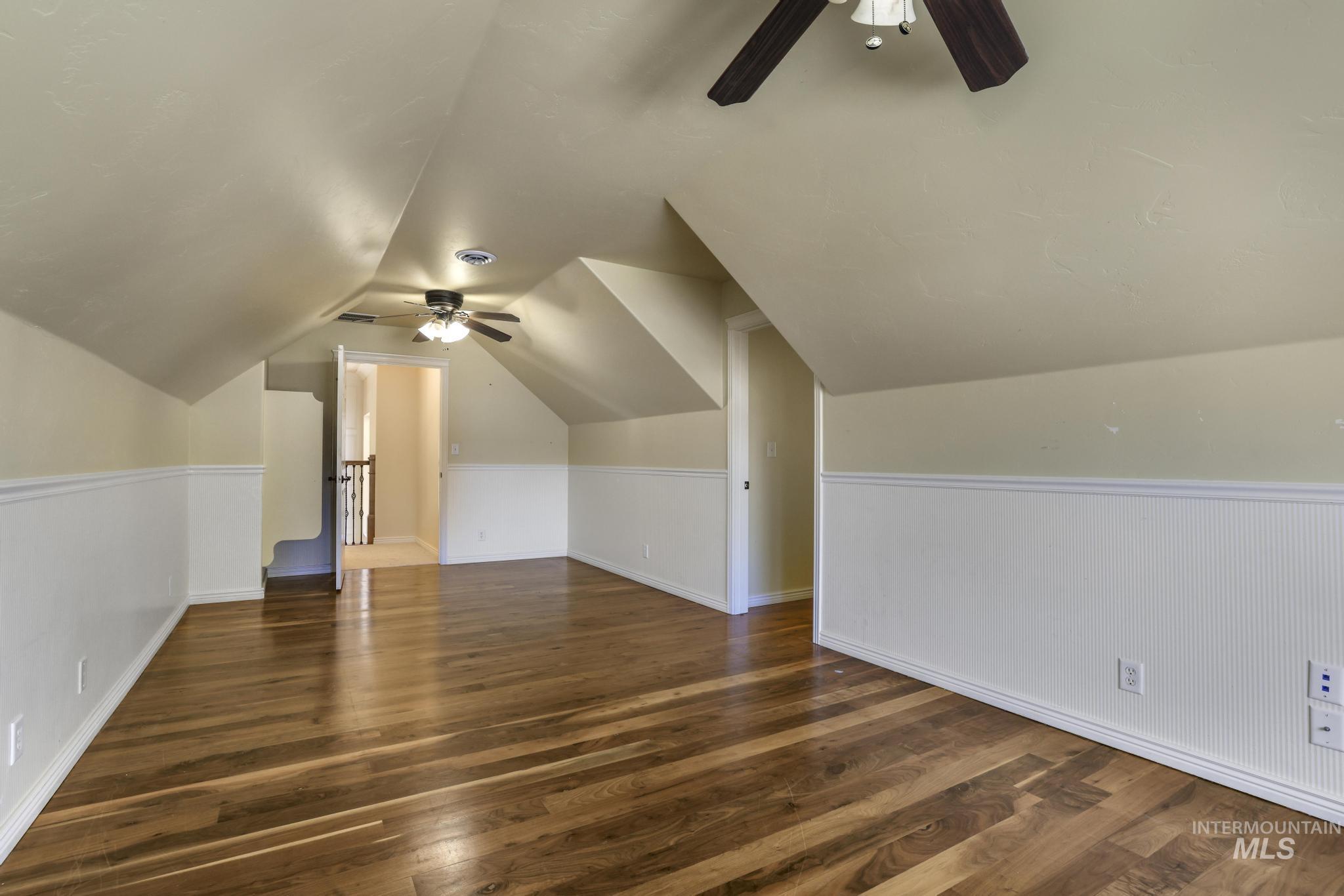 Bonus room with ceiling fan, wainscoting, dark wood-style floors, and lofted ceiling