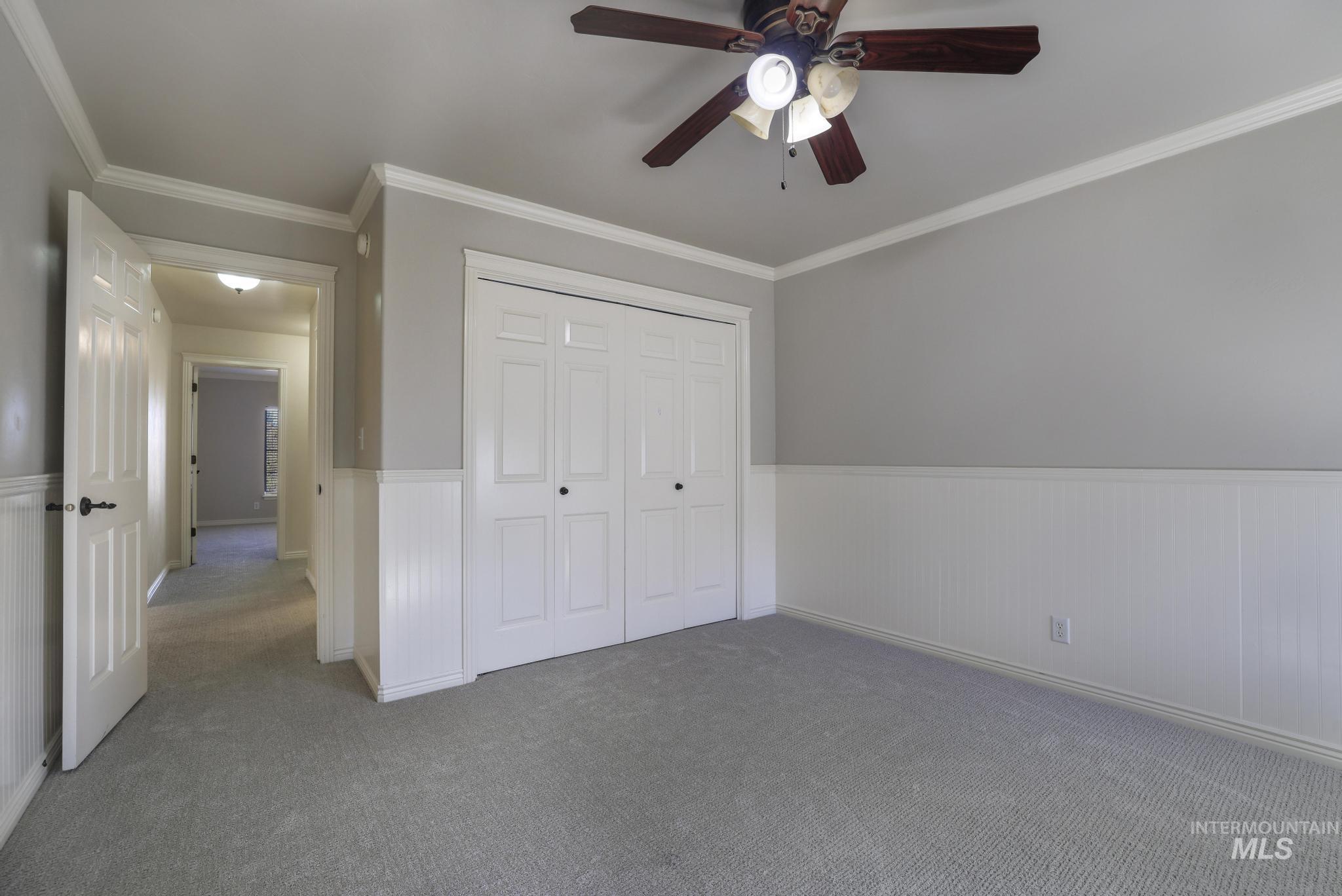 Unfurnished bedroom with ornamental molding, a closet, a wainscoted wall, carpet, and ceiling fan