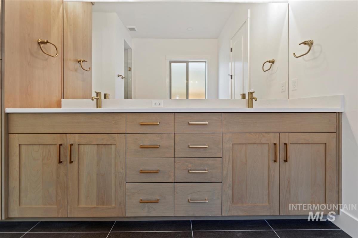 Double vanity featuring light wood-finish cabinetry, white countertops, and dual gold-tone fixtures