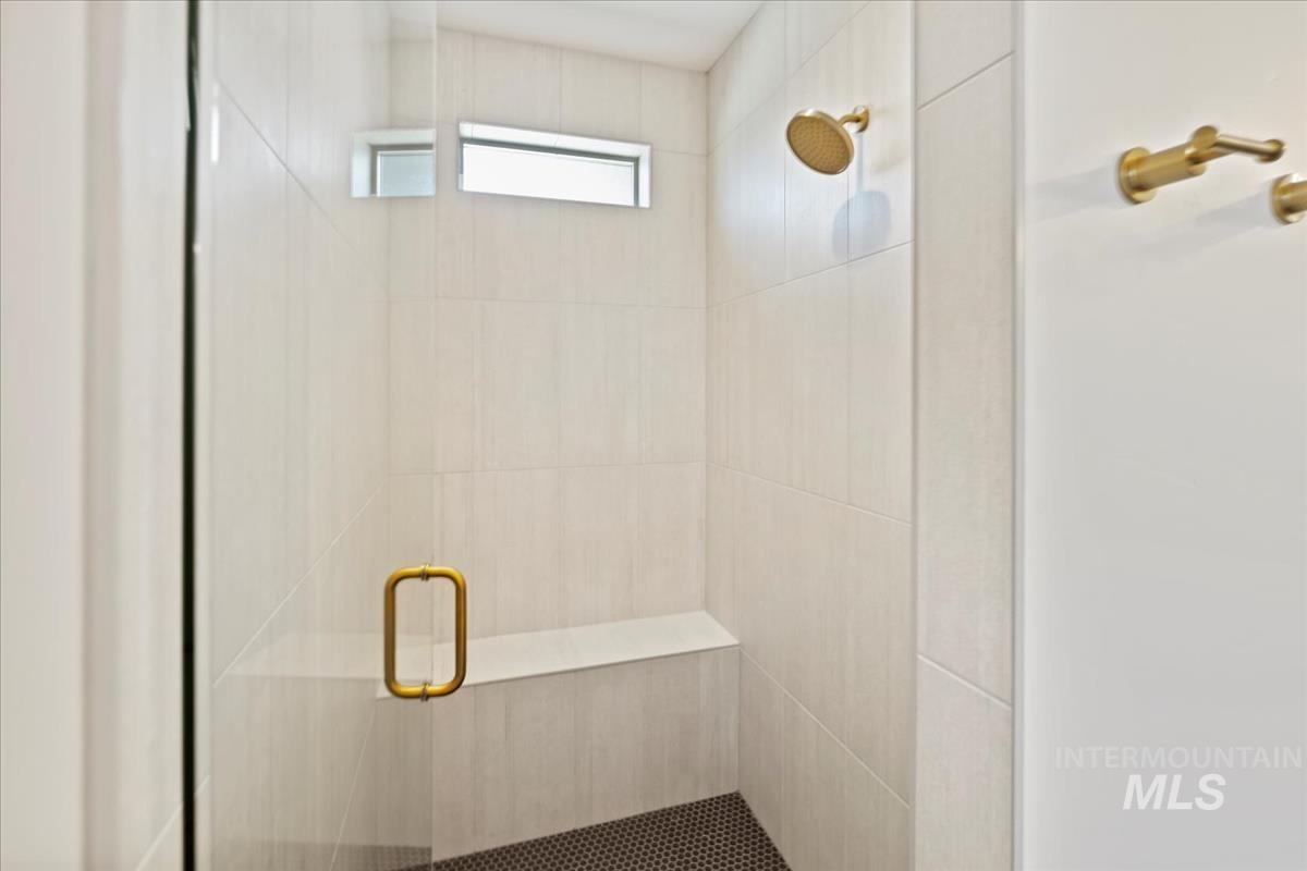 Walk-in shower featuring light-toned large format wall tile, a built-in bench, and a dark tile shower pan