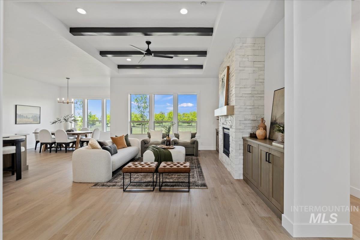 Spacious open-concept living area featuring wood-finish flooring, a contemporary fireplace with stone surround, and an integrated ceiling fan