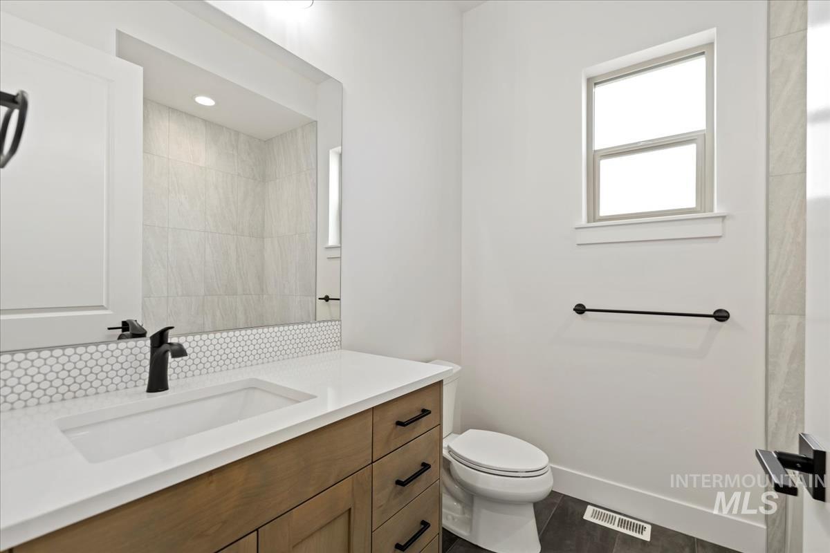 Bathroom featuring a wood-finish vanity with a white countertop and integrated sink, matte black faucet, and hexagon tile backsplash