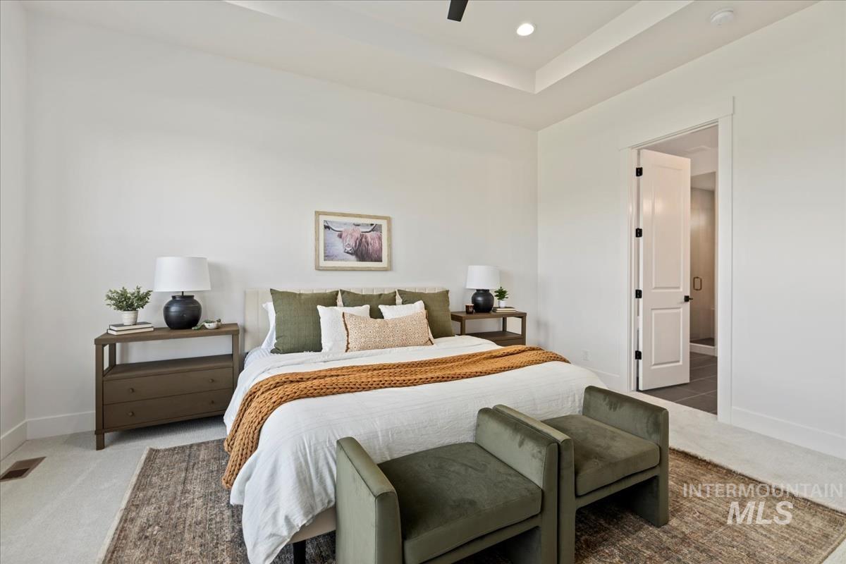 Spacious bedroom featuring a recessed ceiling, ceiling fan, and carpet flooring