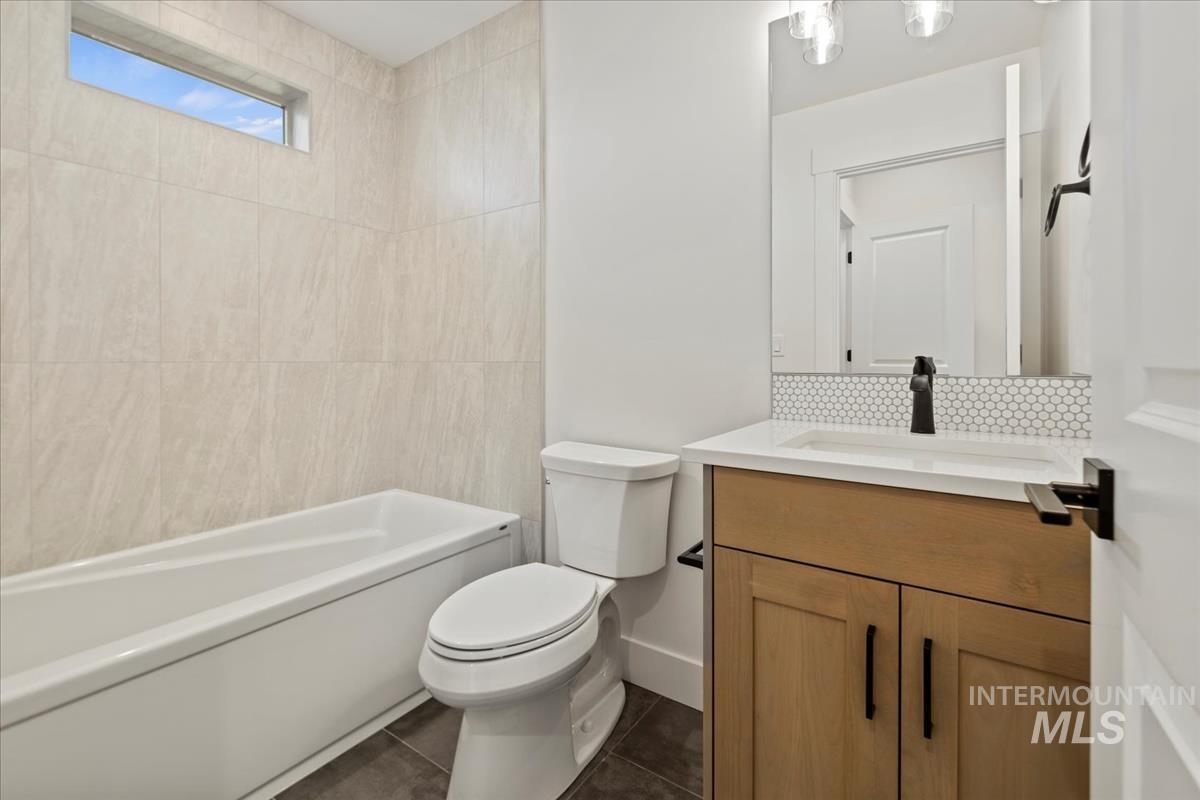Bathroom featuring a white bathtub, a single vanity with wood-finish cabinetry, a white countertop, and a matte black faucet