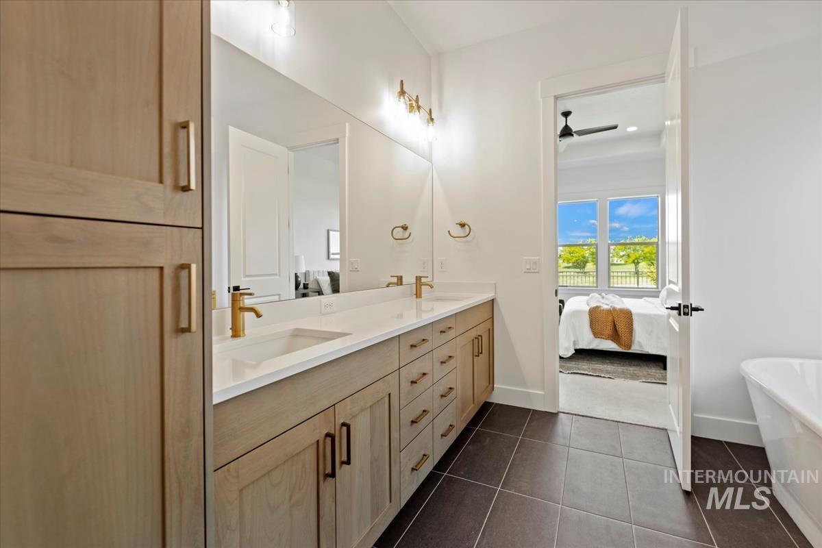 Bathroom featuring a double vanity with light wood-finish cabinetry, white countertop, and gold-tone fixtures