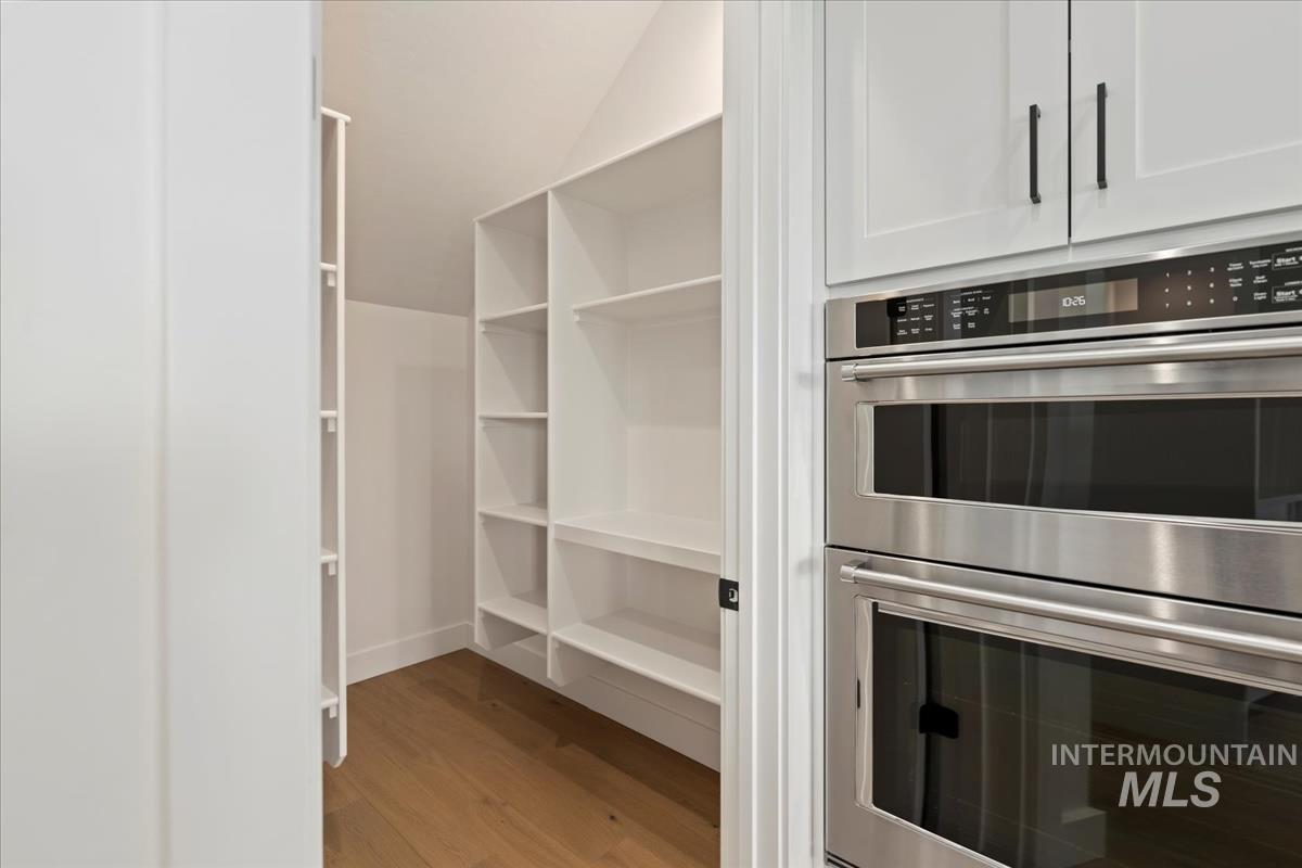 Spacious pantry featuring extensive built-in shelving, wood-finish flooring, and a sloped ceiling