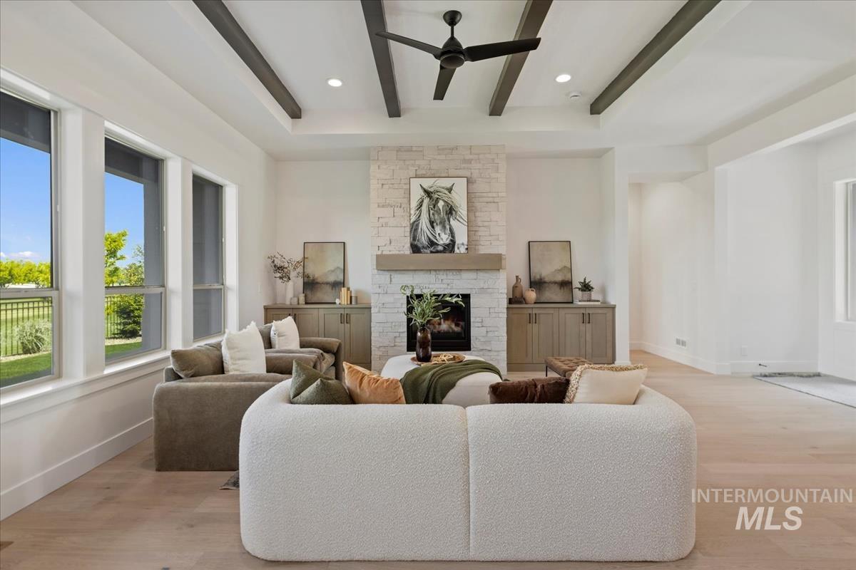 Living area featuring a stone-clad fireplace with a wood mantel, exposed ceiling beams, and a ceiling fan