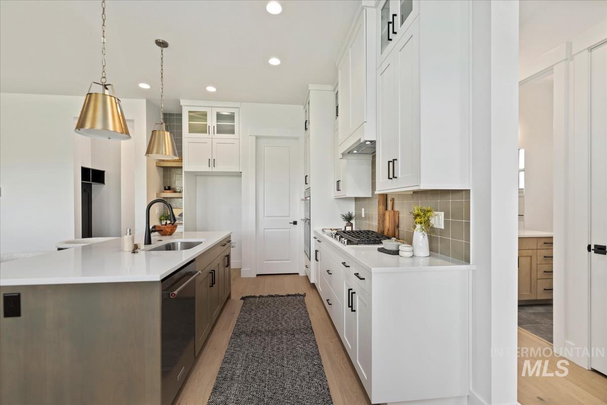 Contemporary kitchen featuring a large island with an integrated sink and dishwasher, white shaker-style cabinetry, light-toned wood-finish flooring, and a gas cooktop