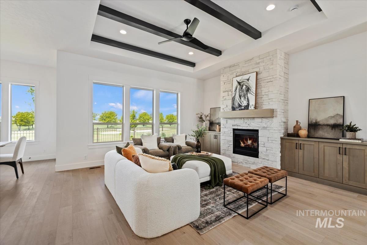 Spacious living area featuring a stone-clad fireplace with a built-in mantel, exposed ceiling beams, and wood-finish flooring