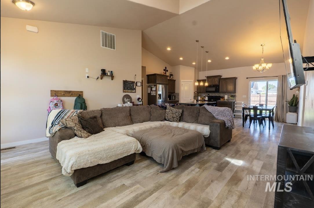 Living room with light wood finished floors, high vaulted ceiling, a chandelier, and recessed lighting