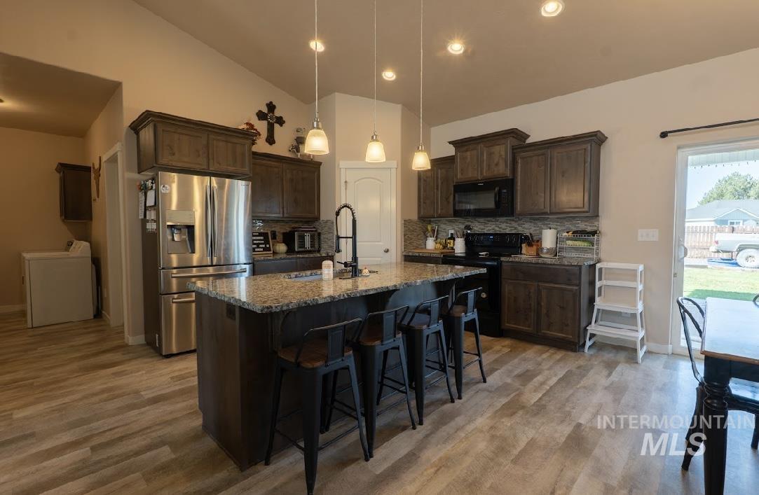 Kitchen with dark brown cabinets, black appliances, a breakfast bar area, tasteful backsplash, and pendant lighting
