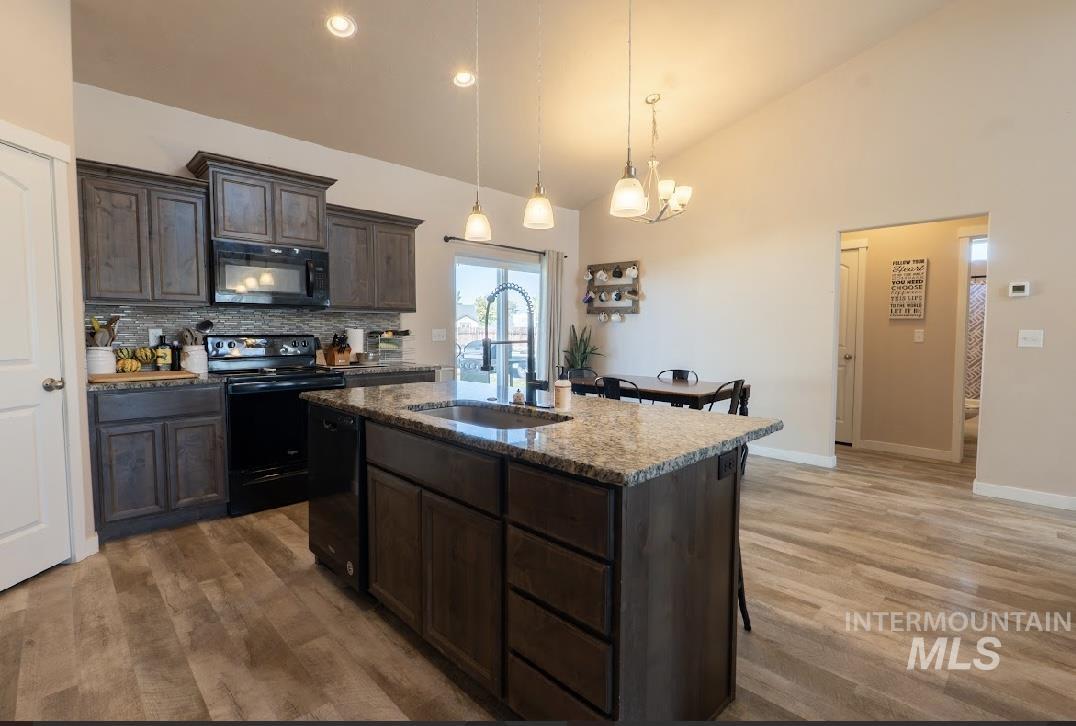 Kitchen with black appliances, backsplash, a center island with sink, decorative light fixtures, and dark brown cabinetry