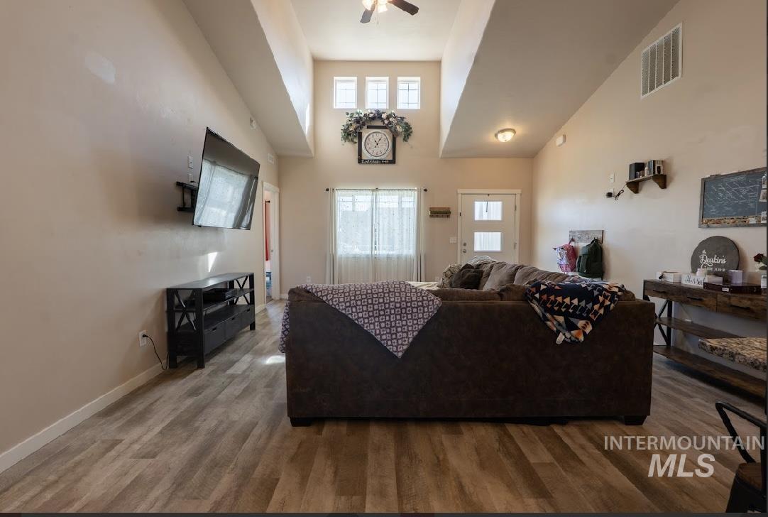 Living room with a high ceiling, wood finished floors, and a ceiling fan