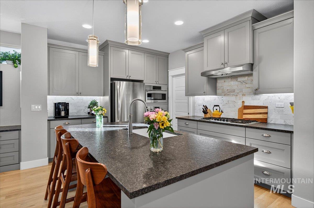 Kitchen featuring gray cabinetry, light wood finished floors, decorative light fixtures, stainless steel appliances, and dark stone countertops