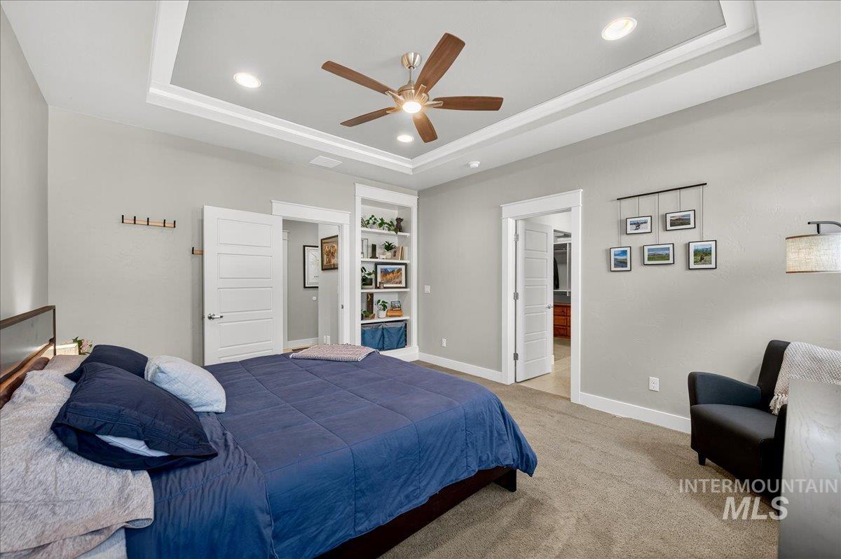 Carpeted bedroom featuring a raised ceiling, recessed lighting, and a ceiling fan