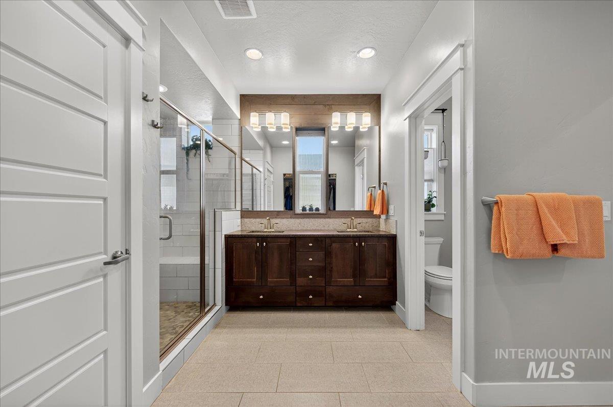 Bathroom featuring a stall shower, double vanity, a textured ceiling, recessed lighting, and light tile patterned floors