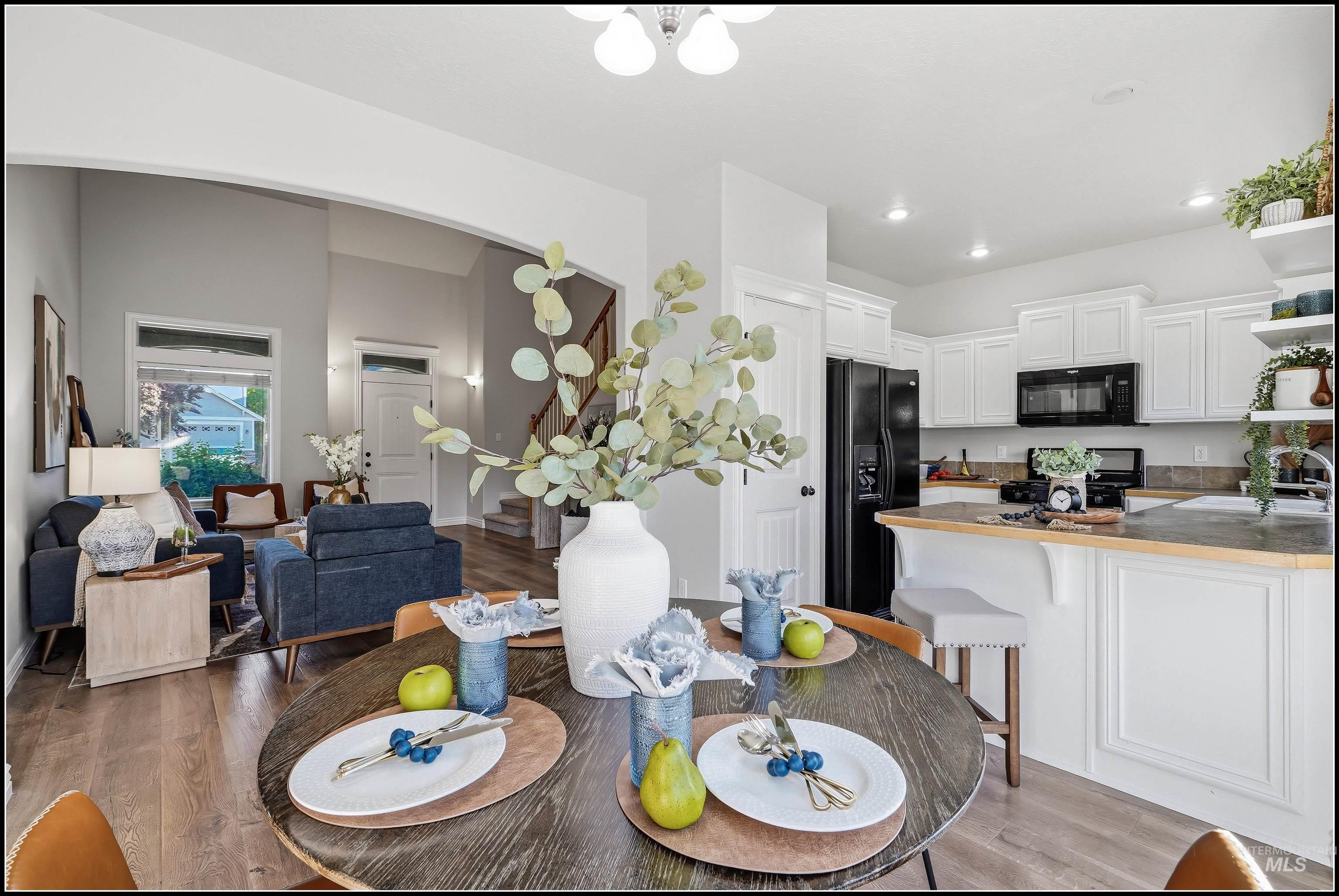 Open-concept living space featuring a dining area, a kitchen with white cabinetry, and a living room with vaulted ceilings