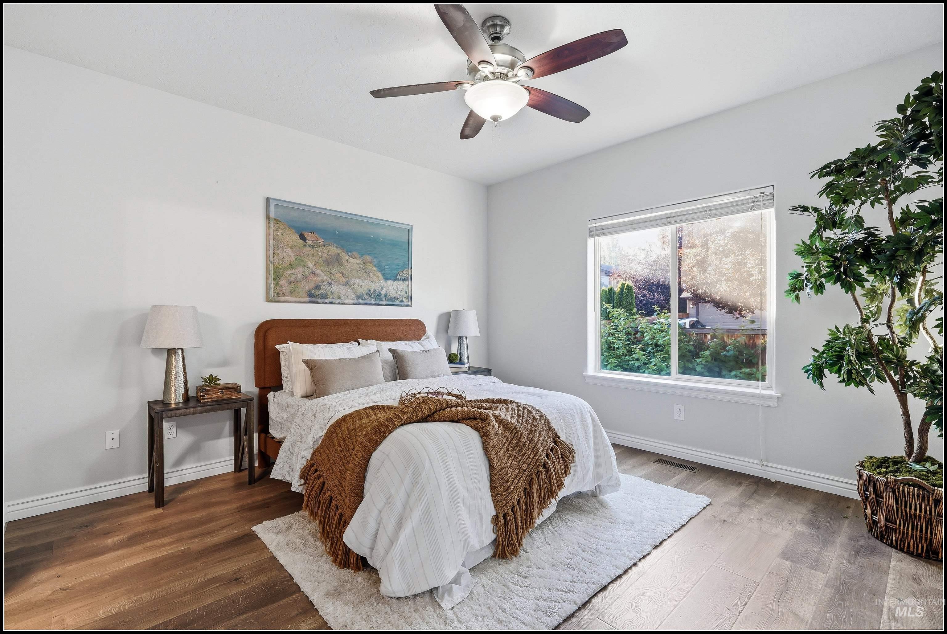 Spacious room featuring wood-finish flooring, a large window with natural light, and a ceiling fan