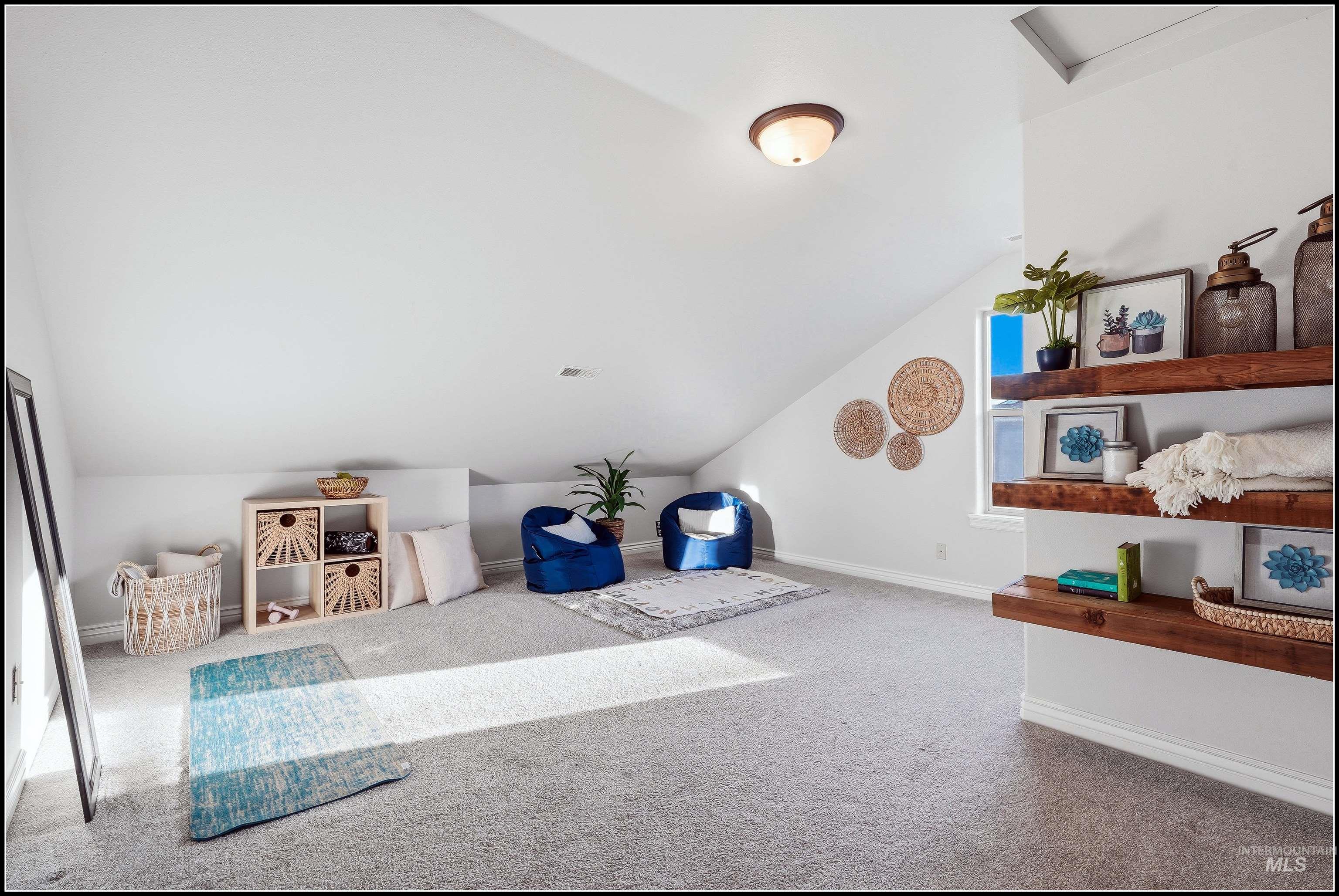 Carpeted loft space featuring built-in wooden shelving, an angled vaulted ceiling, and a window