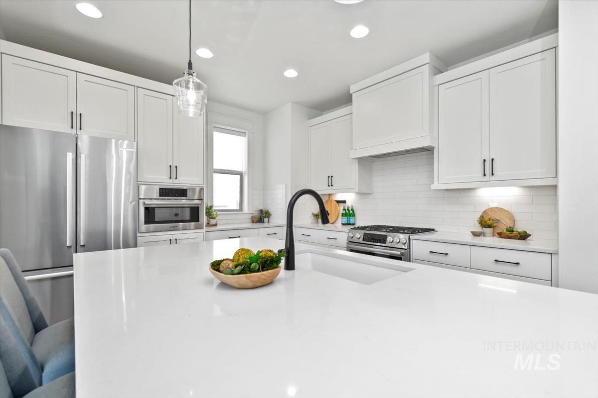 Kitchen with stainless steel appliances, light countertops, recessed lighting, white cabinetry, and hanging light fixtures