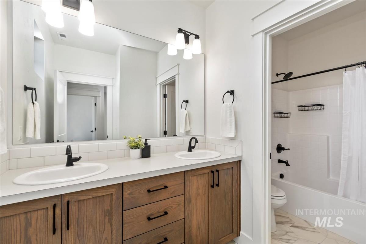 Full bath with double vanity, marble finish flooring, and shower / bathtub combination with curtain