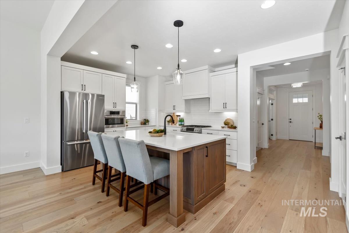 Kitchen with appliances with stainless steel finishes, light wood-style floors, tasteful backsplash, light countertops, and a kitchen bar