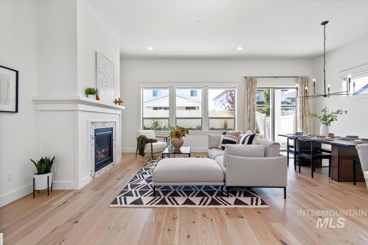 Living area with light wood finished floors, plenty of natural light, a chandelier, a glass covered fireplace, and recessed lighting