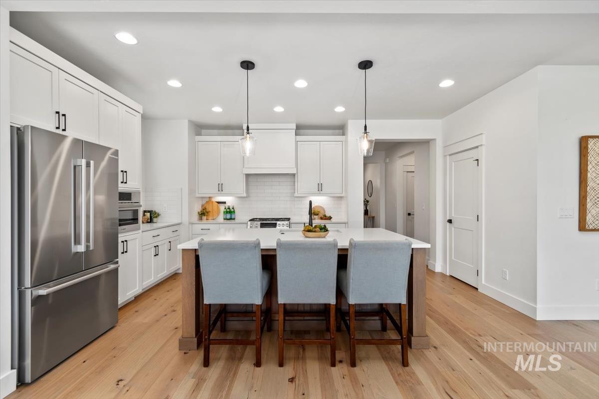 Kitchen with stainless steel appliances, light countertops, light wood finished floors, white cabinets, and recessed lighting