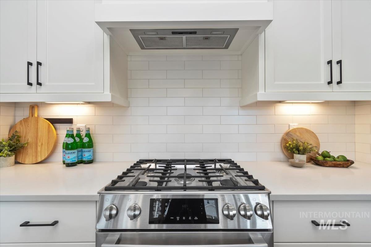 Kitchen with range hood, stainless steel gas range oven, light countertops, and white cabinetry